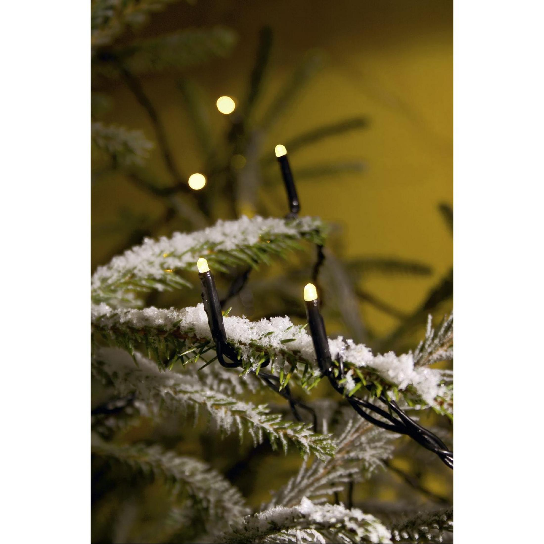 Weihnachtsbeleuchtung auf einem verschneiten Ast. Die Lichter sind weiß und der Hintergrund gelb.