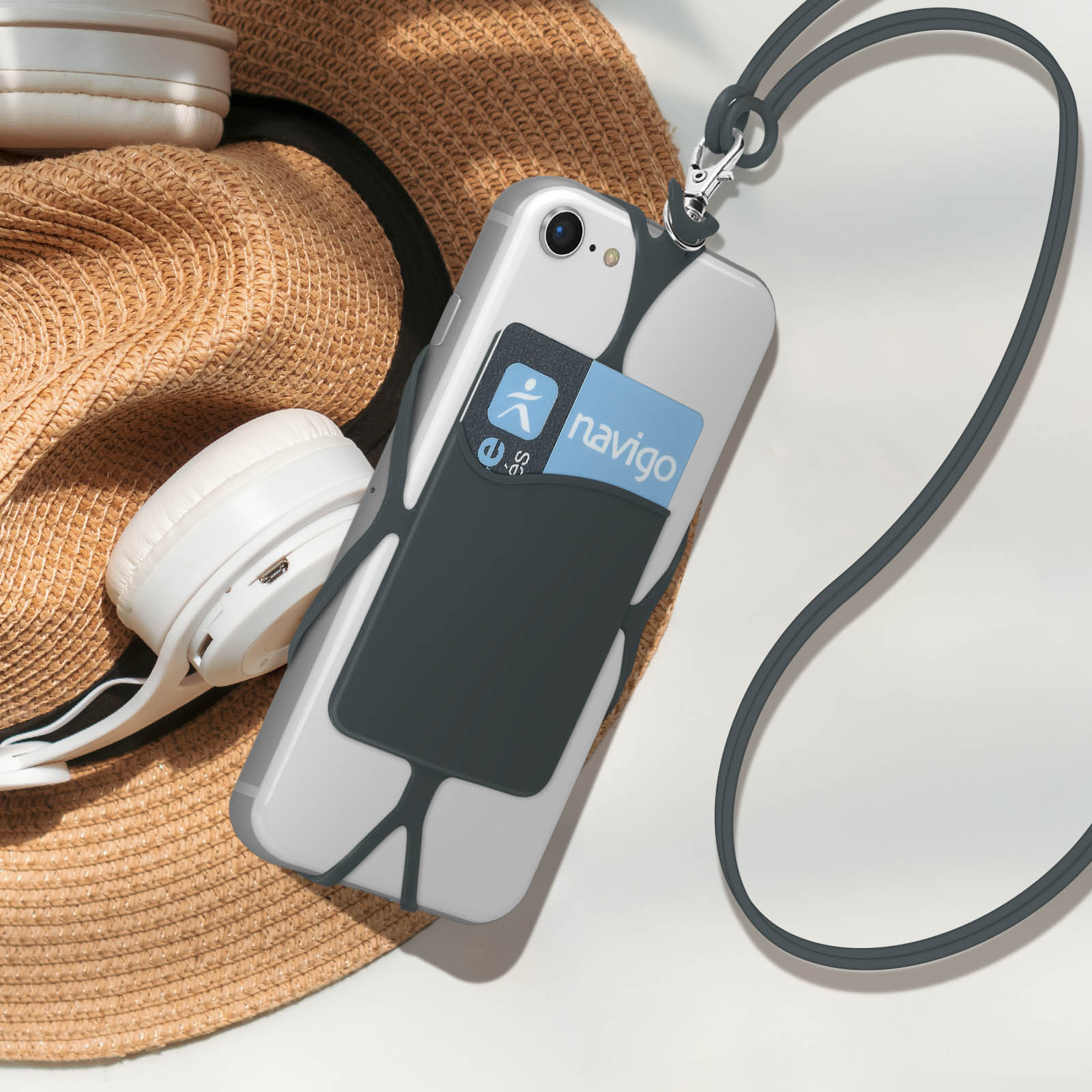 Telefono con porta carte, cordino e cappello su superficie bianca. Cuffie sullo sfondo.