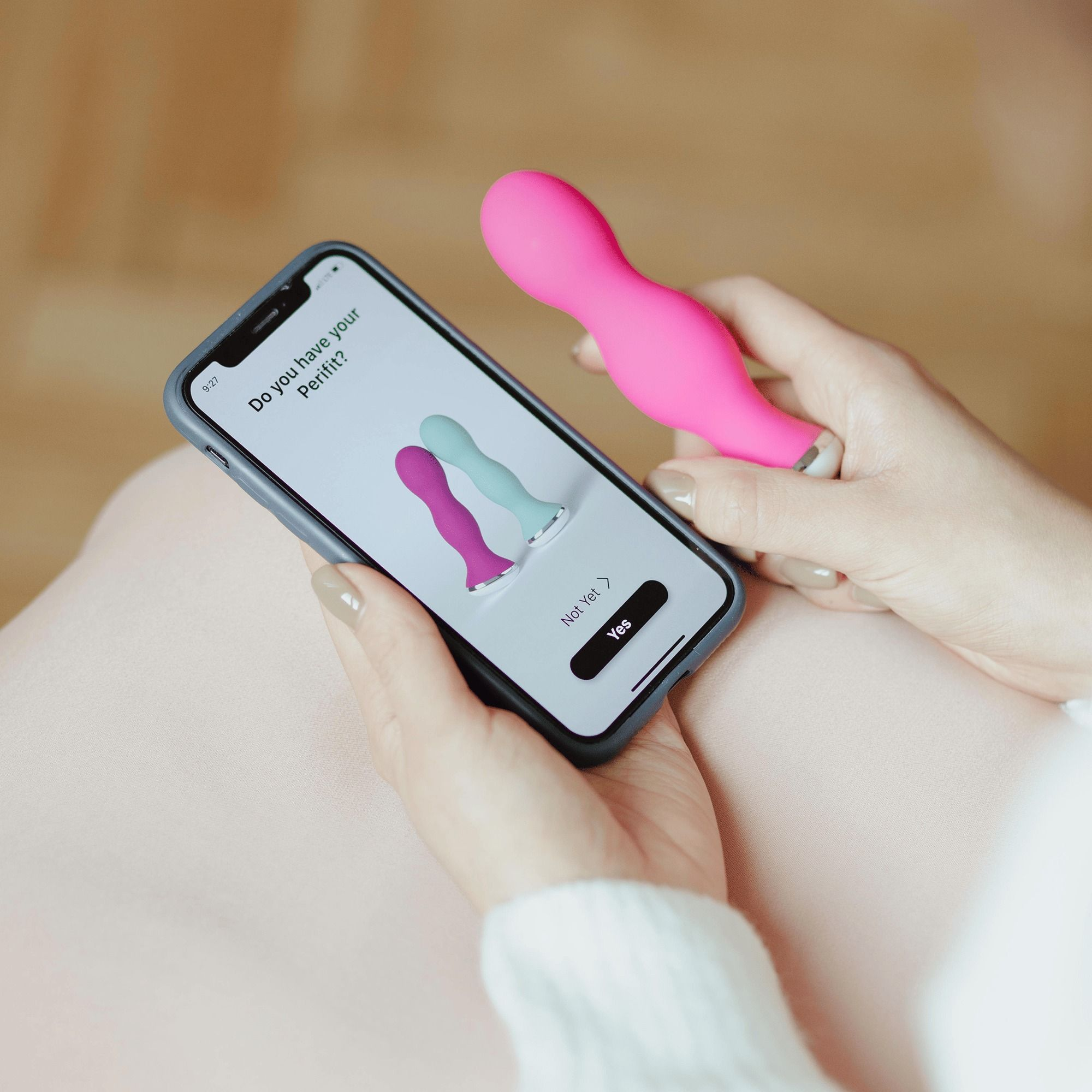 Eine Hand hält ein Smartphone mit App, während die andere Hand ein pinkes Gerät hält.