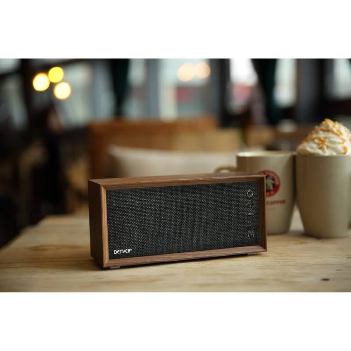 Altavoz marrón y negro sobre una mesa de madera. Hay dos tazas detrás del altavoz.