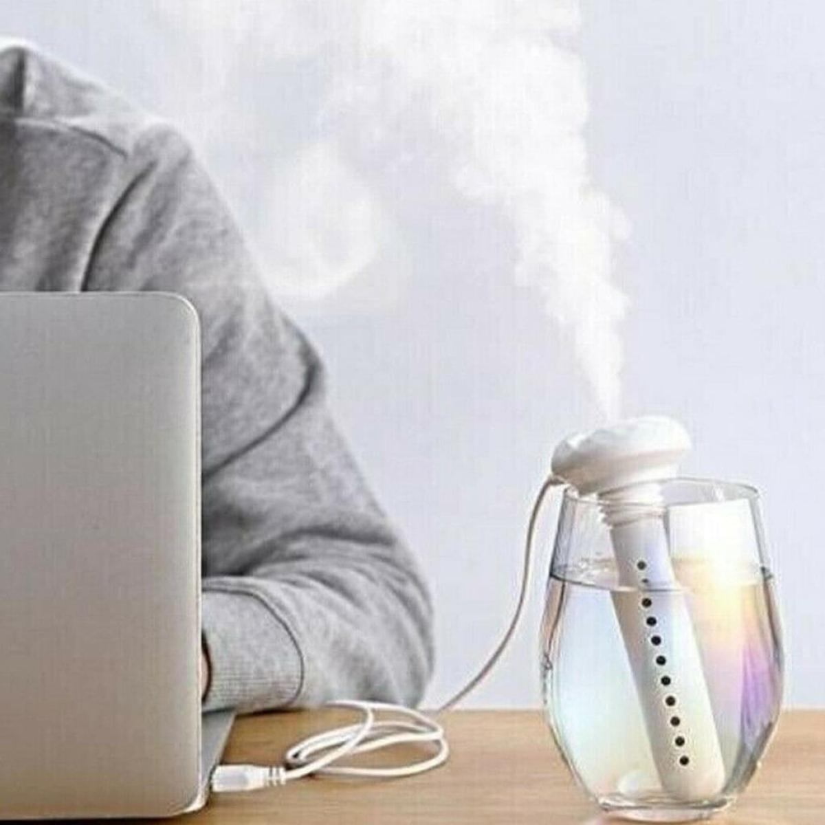 Luftbefeuchter in einem Glas. Eine Person befindet sich neben einem Laptop. Dampf kommt aus dem Befeuchter.