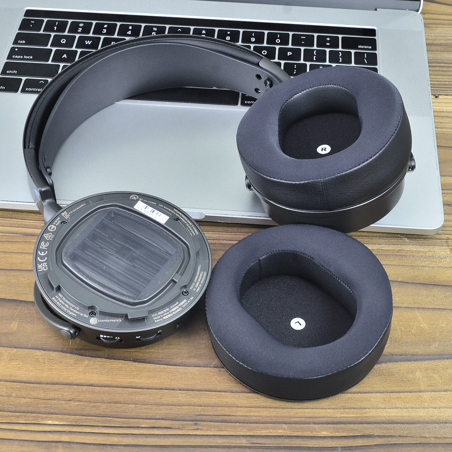 Słuchawki zdemontowane, z nausznikami i korpusem głównym na drewnianej powierzchni, z laptopem.