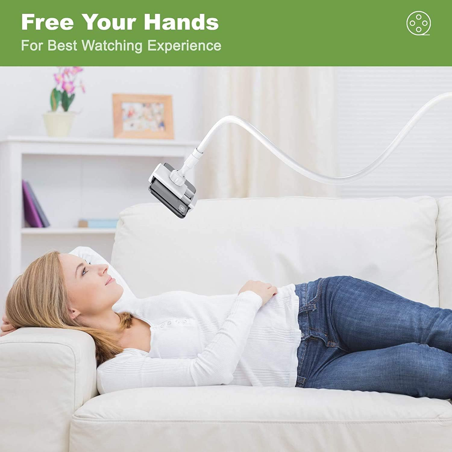 Frau liegt auf weißem Sofa, schaut auf Telefon an flexiblem Arm. Weißer Raum.