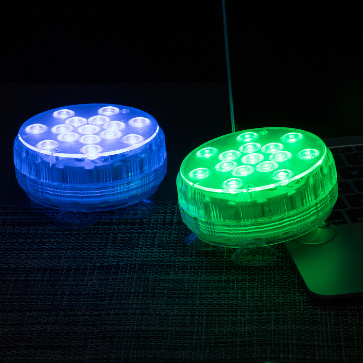 Zwei LED-Leuchten, eine blau, eine grün, auf schwarzem Untergrund. Ein Laptop im Hintergrund sichtbar.