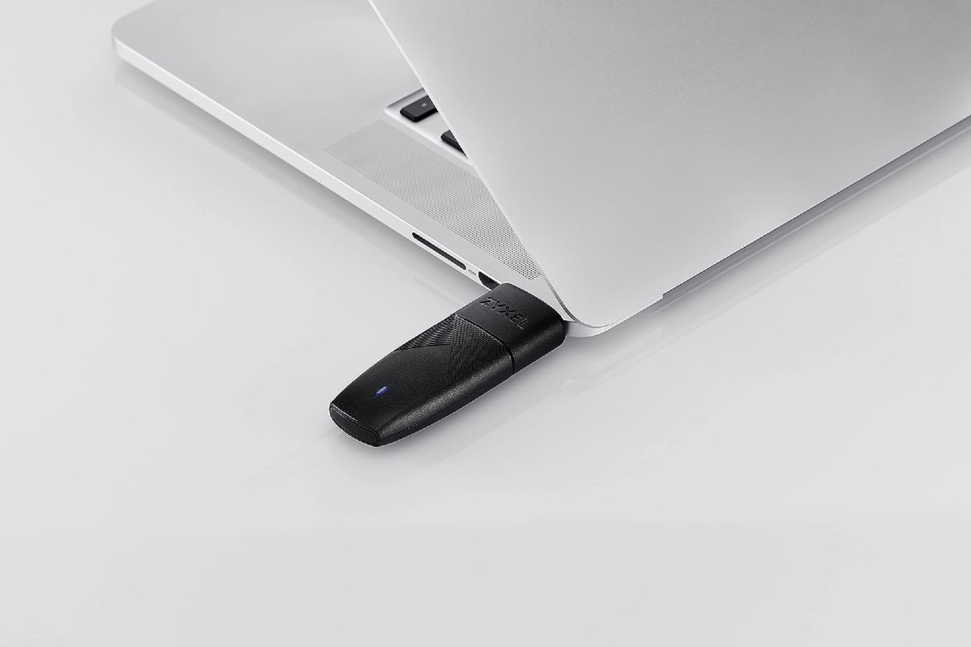 Un dongle USB-C nero collegato a un laptop argento aperto. Il dongle ha una luce blu.
