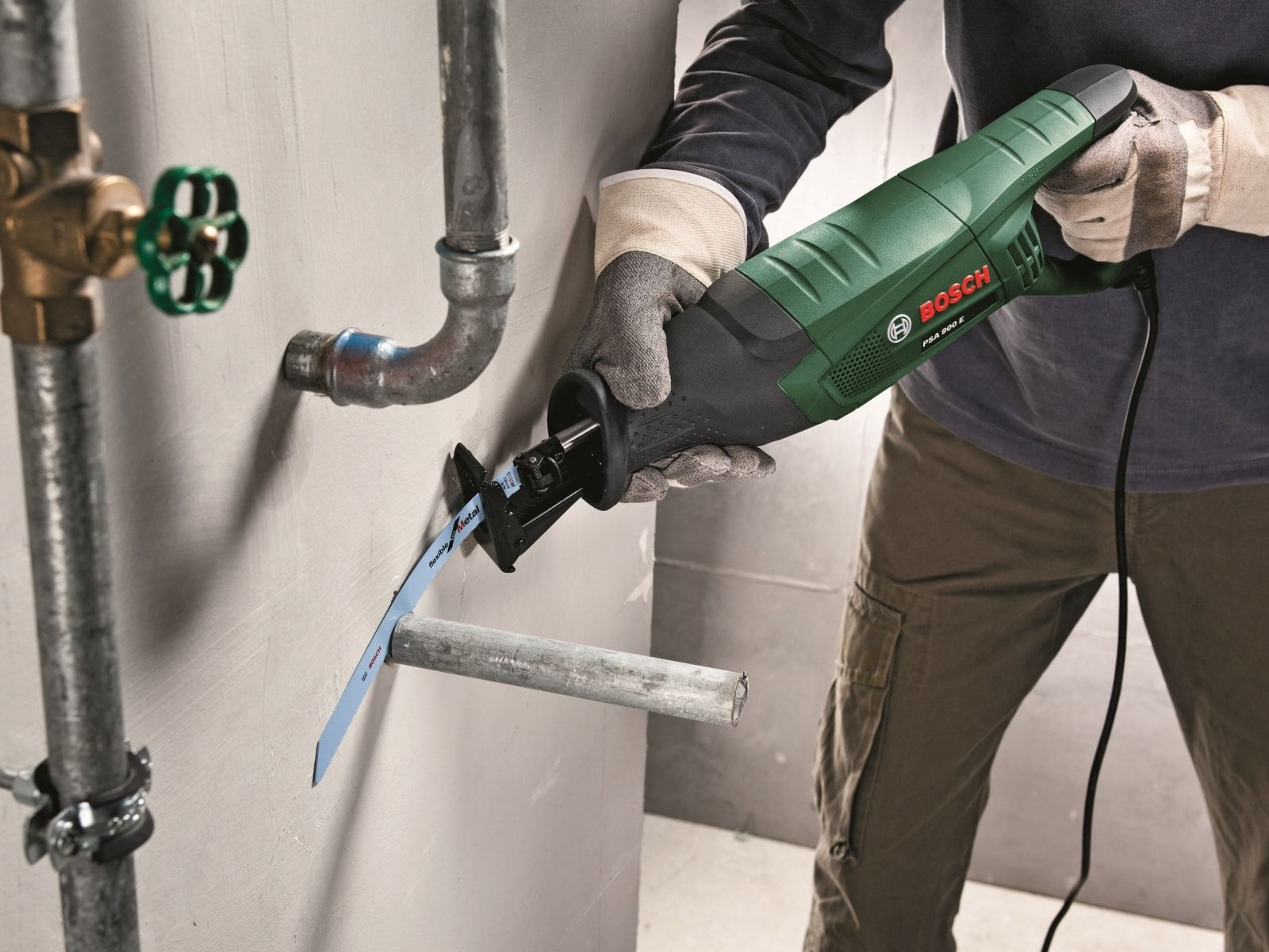 Mężczyzna używa piły do cięcia rury, nosząc rękawice, w środowisku budowlanym.