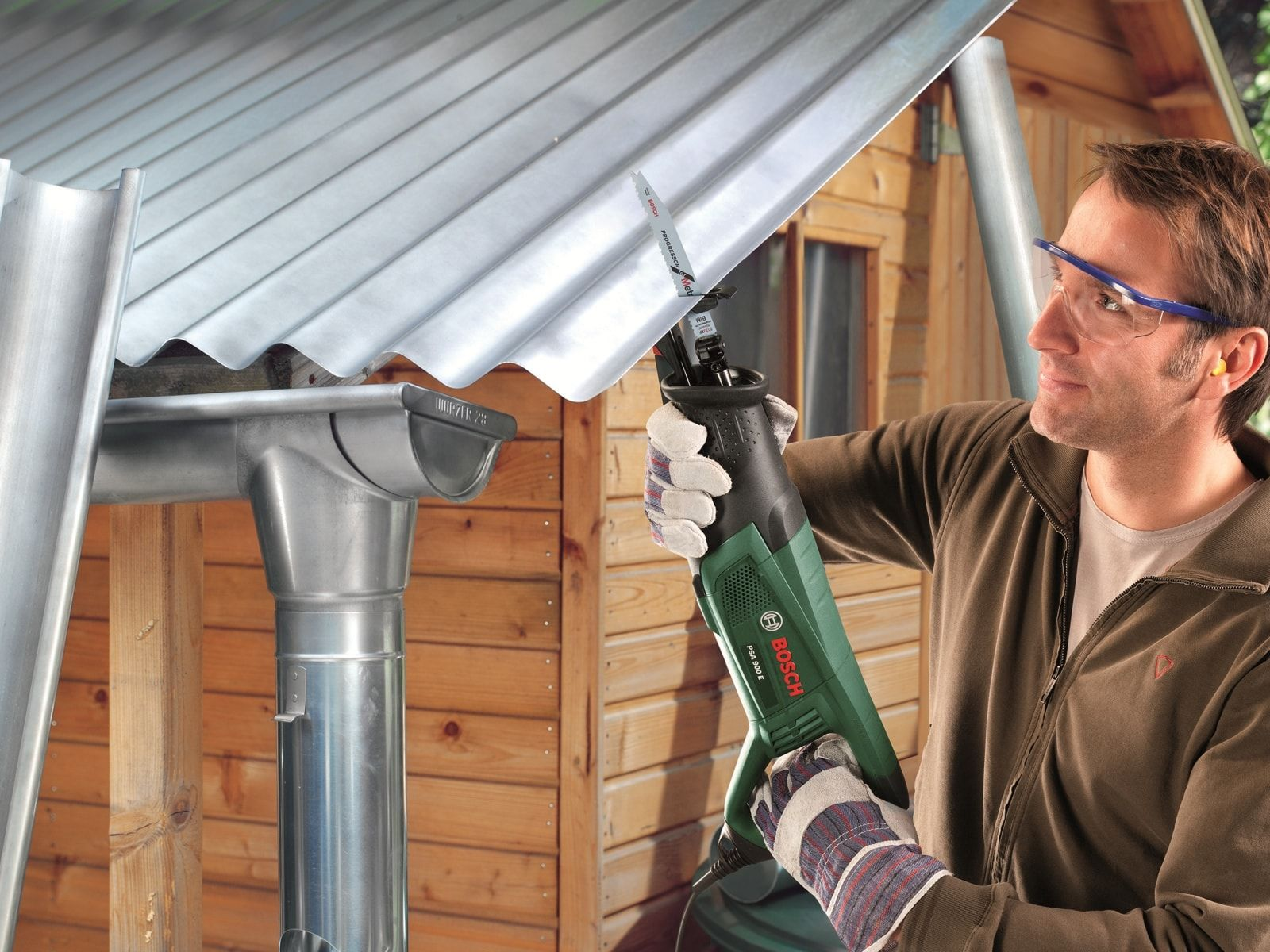 Mężczyzna tnie metalowe pokrycie dachowe piłą elektryczną. Nosi okulary i rękawice ochronne.