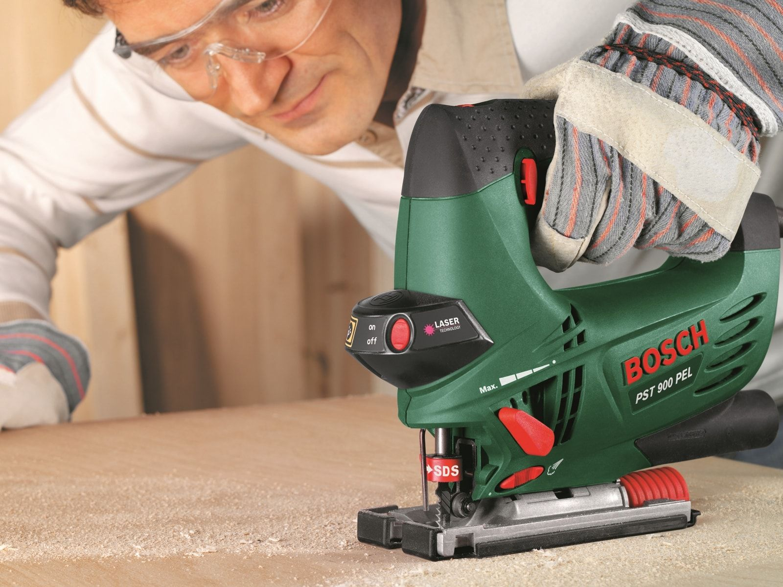 Mężczyzna używający zielono-czarnej wyrzynarki, z drewnianą powierzchnią na pierwszym planie.