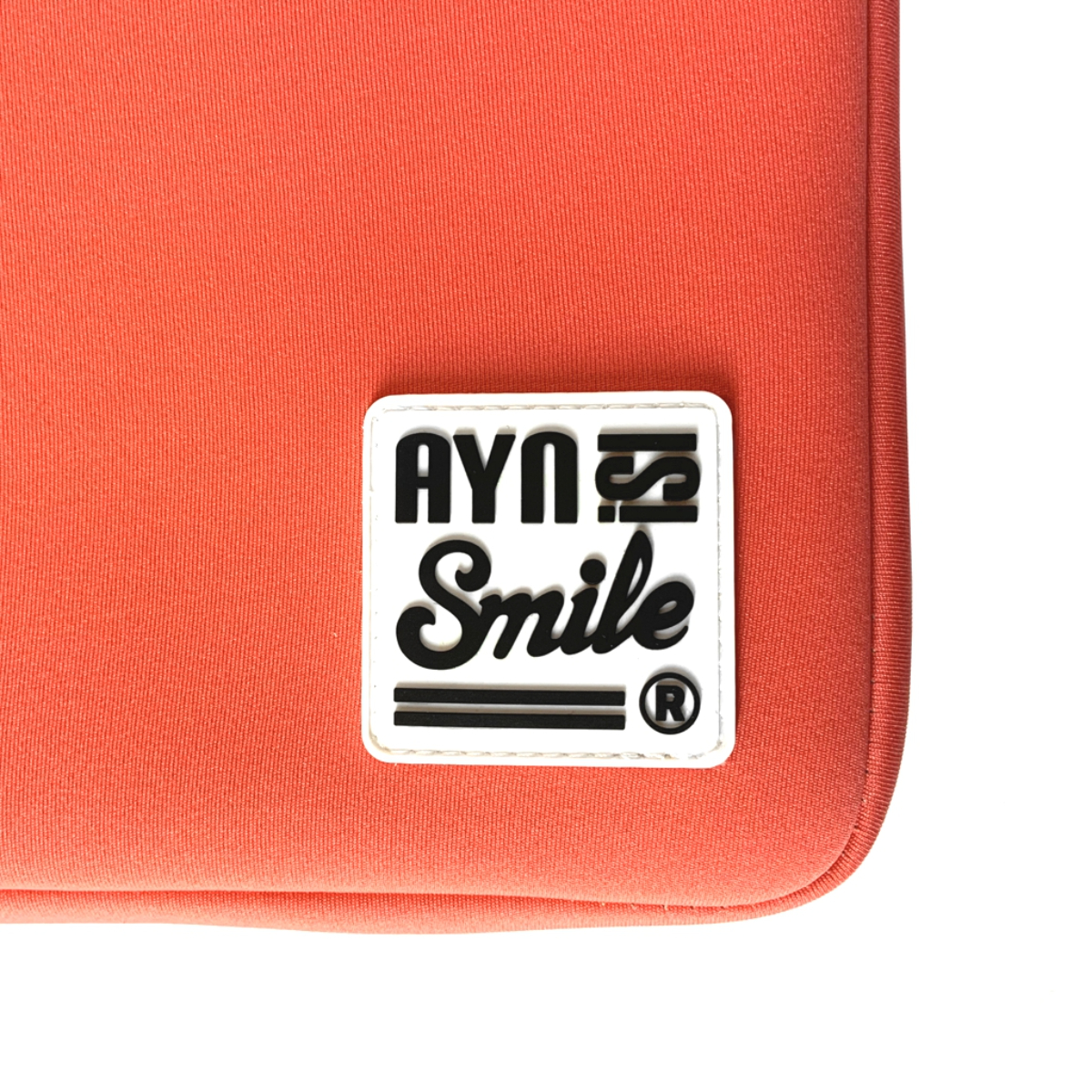 Primer plano de una funda para portátil coral con un parche blanco que tiene el texto 'AYN Smile'.