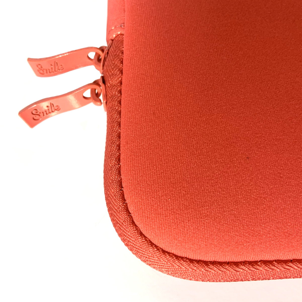Primo piano di una custodia per laptop color corallo con due cerniere con l'etichetta 'Smile' su sfondo bianco.
