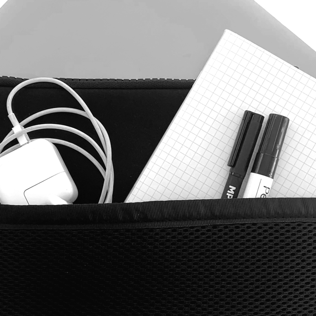 Borsa a rete nera con caricabatterie bianco, quaderno e due pennarelli neri all'interno.