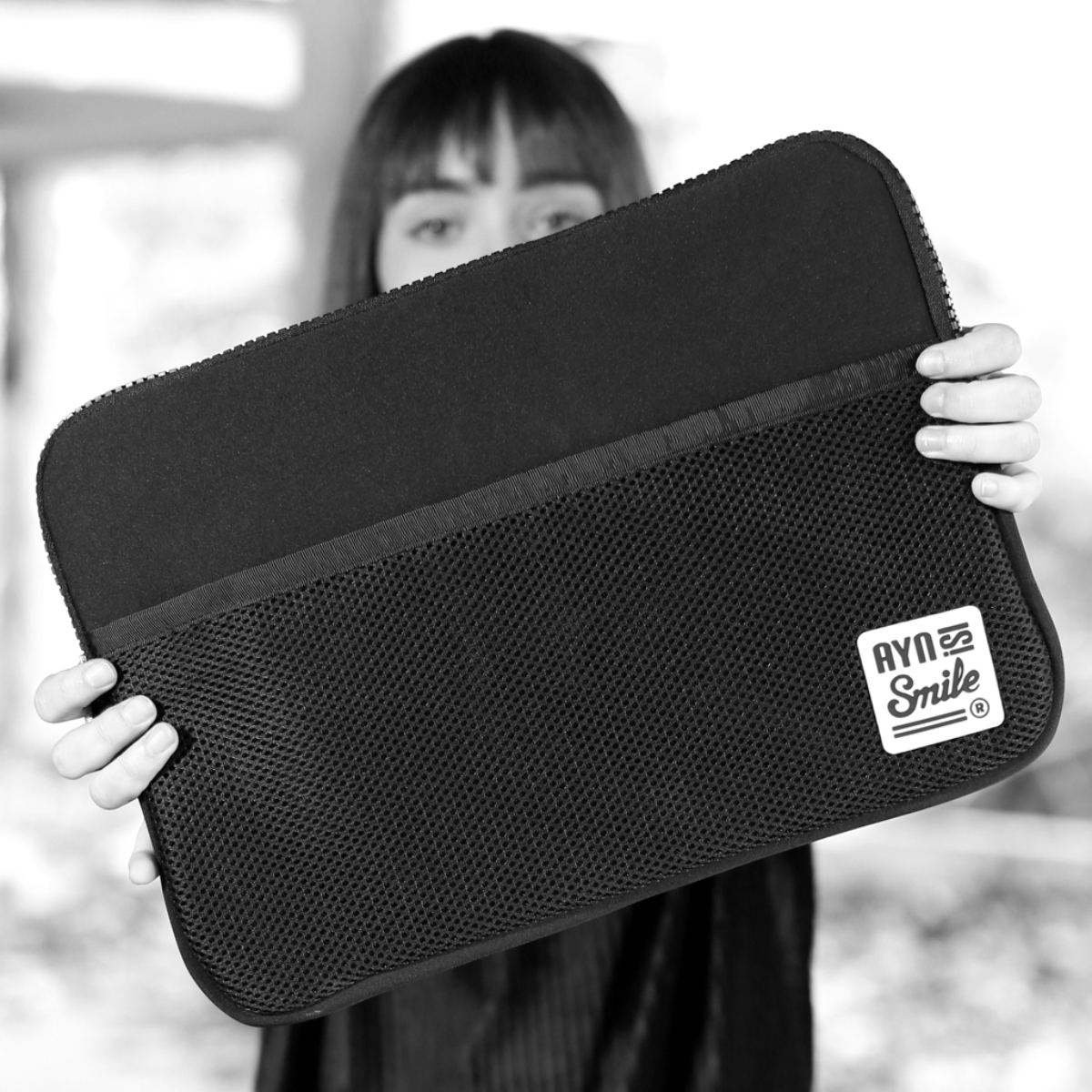 Persona sosteniendo un maletín negro para portátil con logo. Foto en blanco y negro.