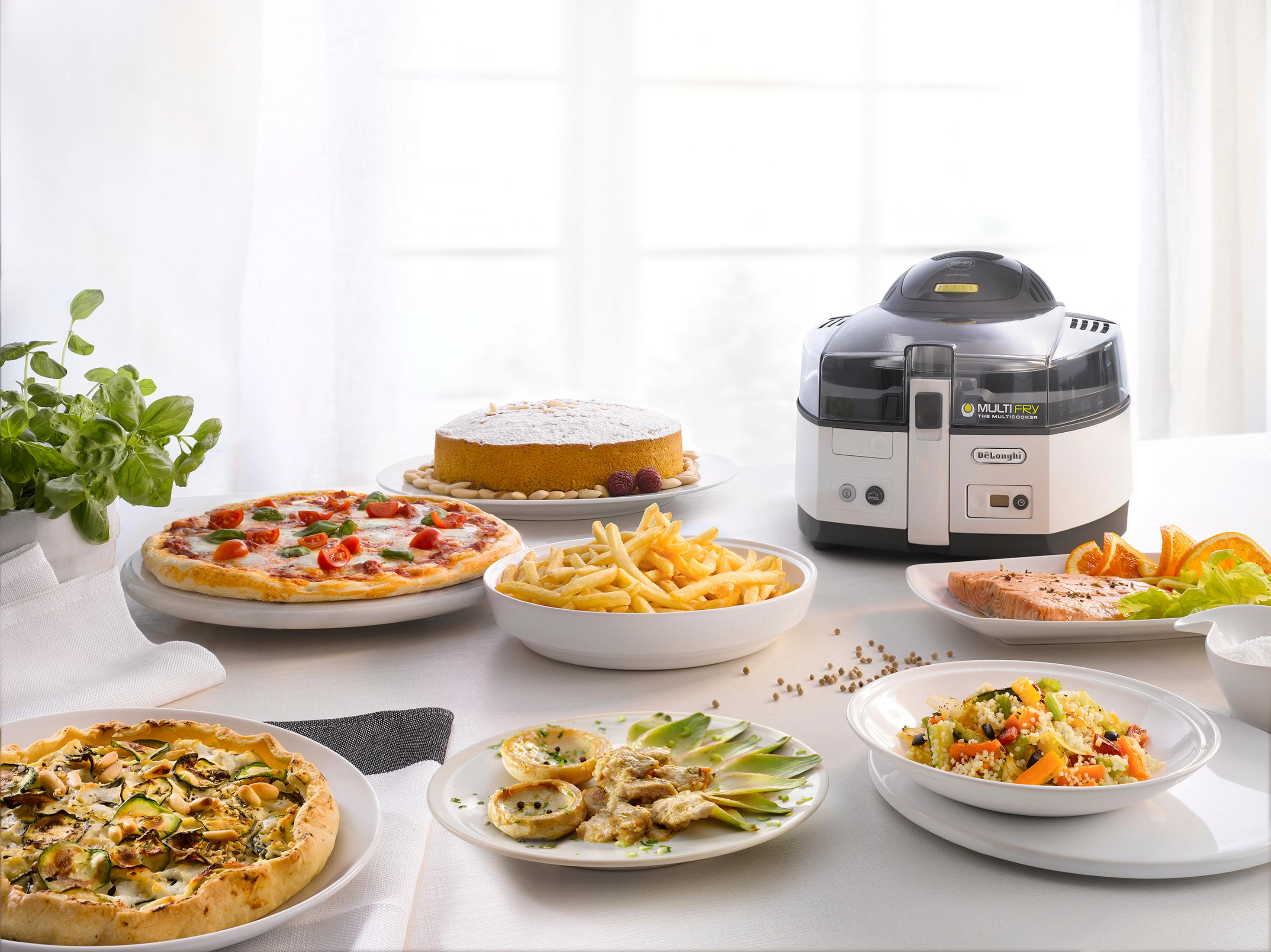 Una mesa con varios platos, incluyendo pizza, papas fritas y un pastel, con un procesador de alimentos.