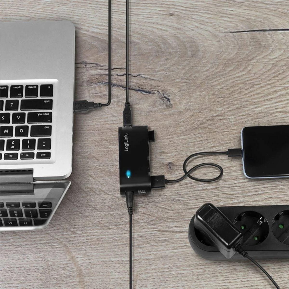 Un hub LogiLink collegato a un laptop, un telefono e una presa di corrente.