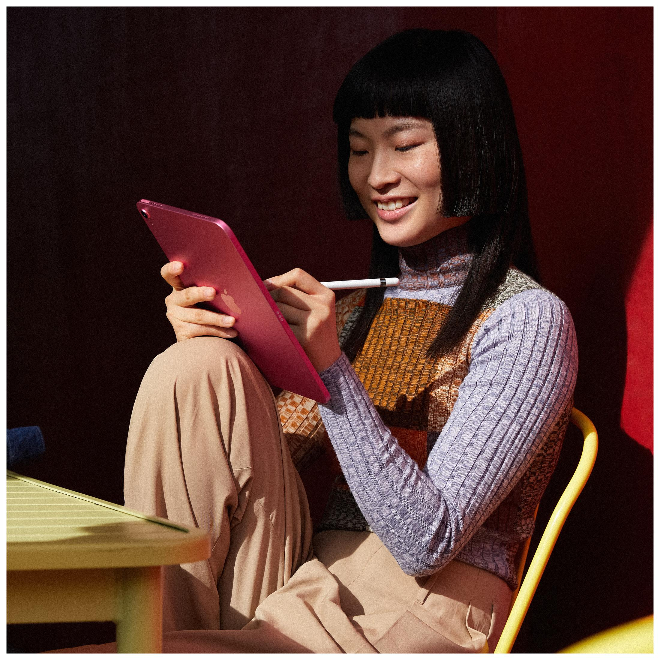 Kobieta siedzi, używa różowego tabletu i białego rysika, uśmiecha się.