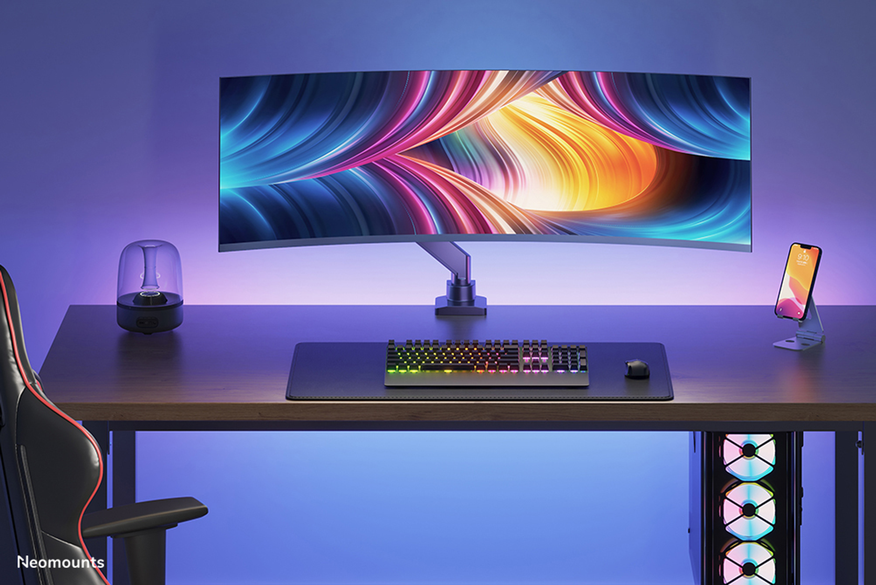 A desk setup featuring a curved monitor, keyboard, mouse, speaker, and smartphone.