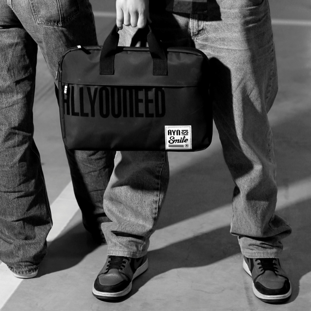 Dos personas con jeans sosteniendo una bolsa negra con la impresión 'ALLYOUNEED' y 'AYA Smile'.