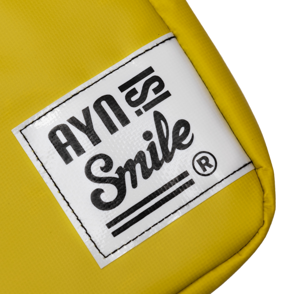 Bolsa amarilla con etiqueta blanca 'AYN Smile'. La etiqueta tiene borde y texto negros.