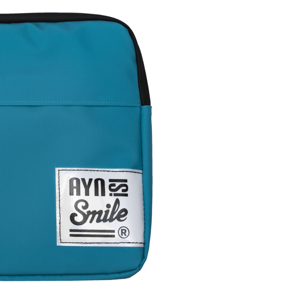 Esquina de bolso color turquesa con etiqueta blanca con texto 'AYNS Smile'. Parte superior negra y fondo blanco.