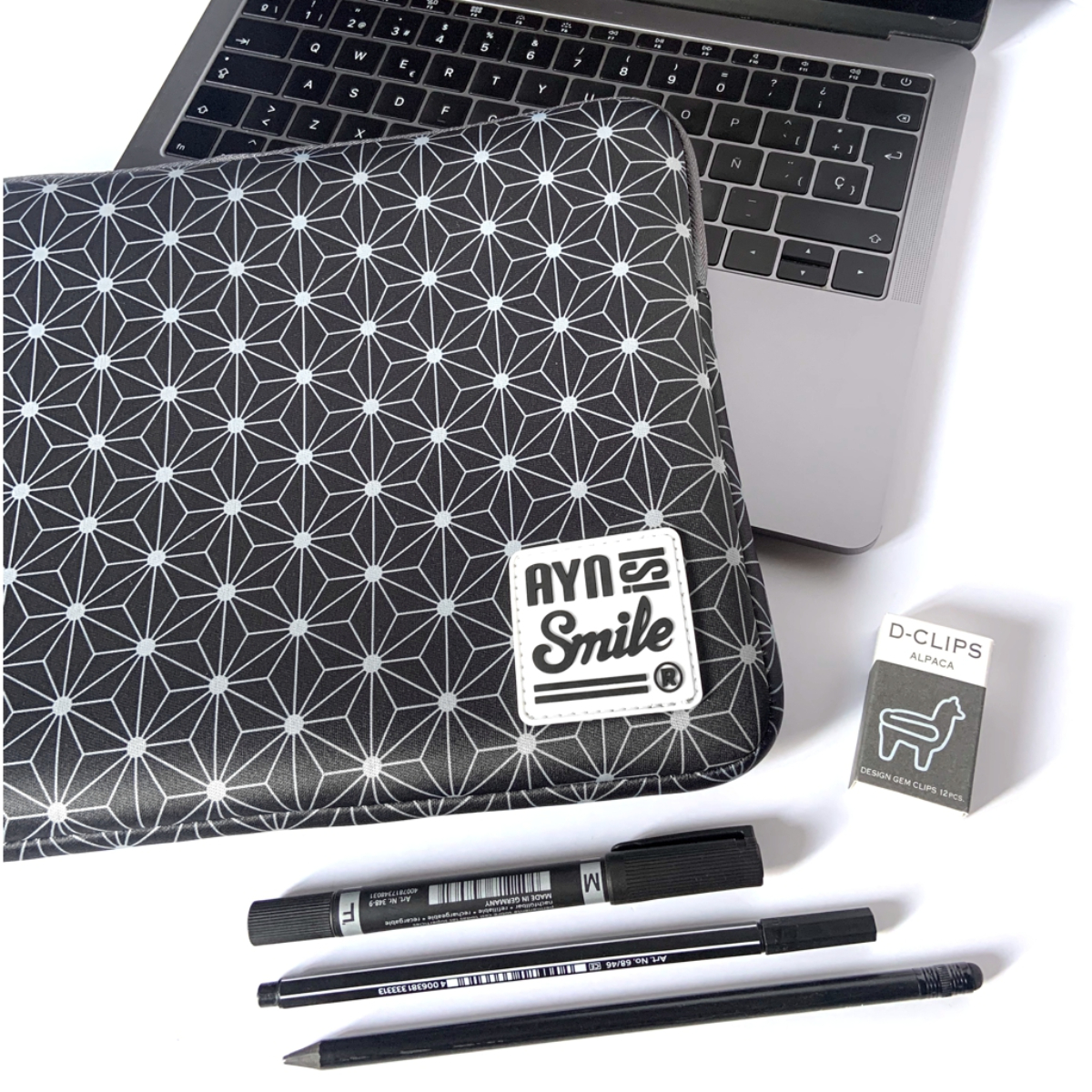 Custodia nera per laptop con motivo geometrico bianco accanto a un Macbook.