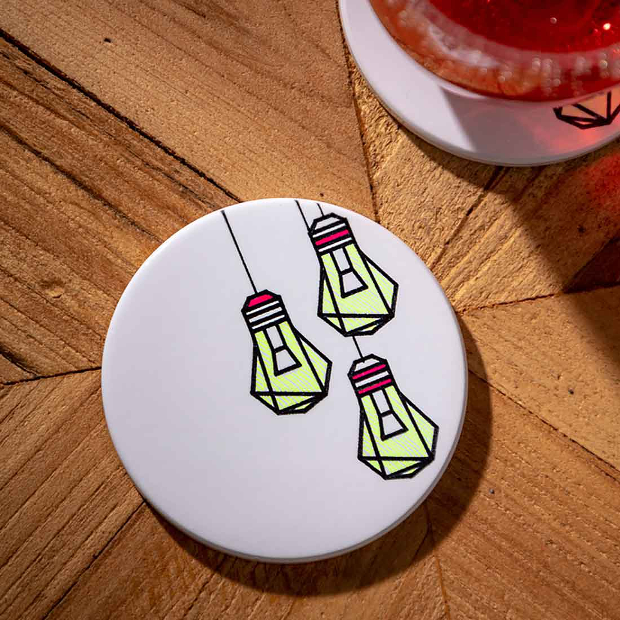 Weiße Untersetzer mit Glühbirnen-Design. Der Hintergrund ist aus Holz. Rechts ist ein Glas.