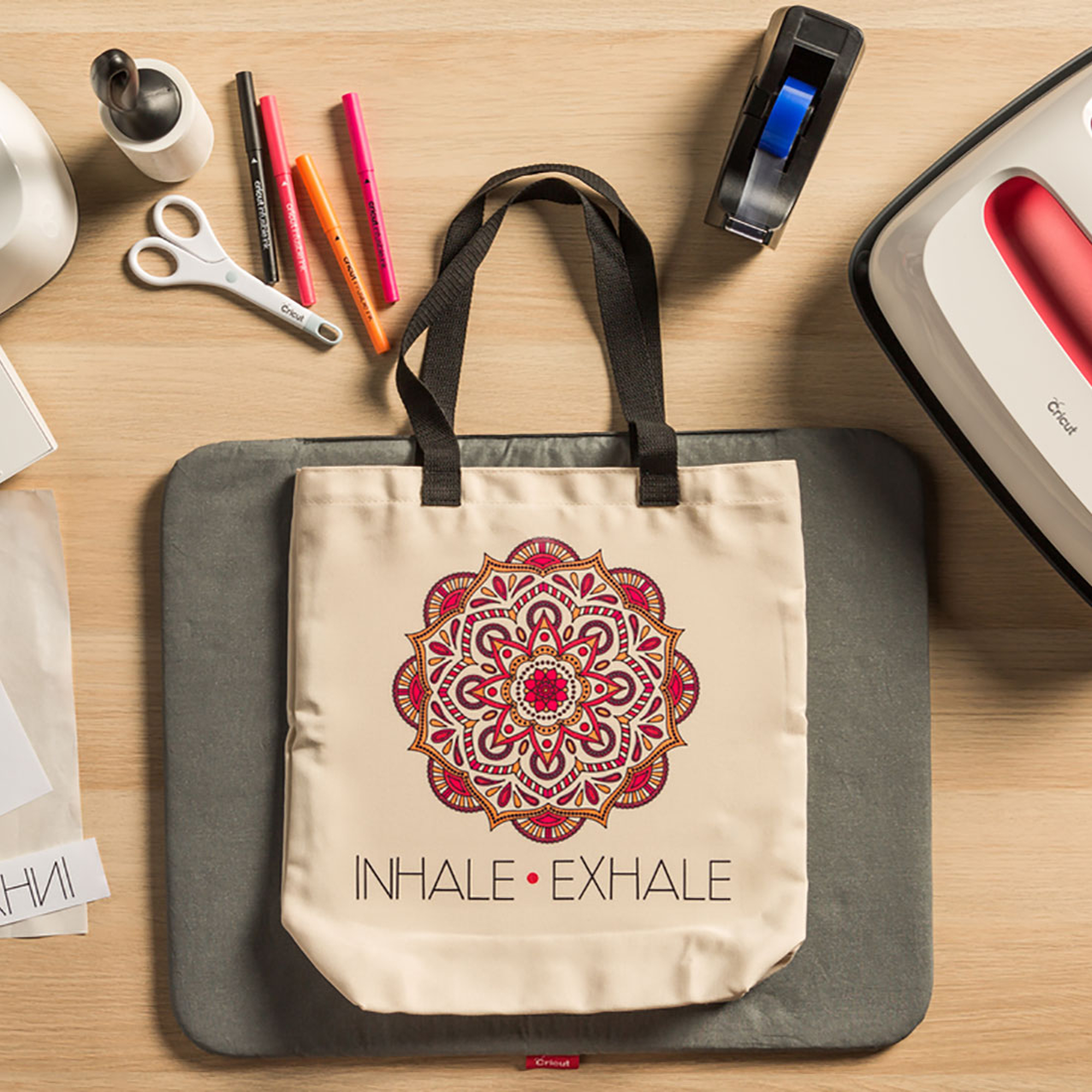 Tragetasche auf grauer Matte mit Mandala-Design, umgeben von Bastelbedarf.
