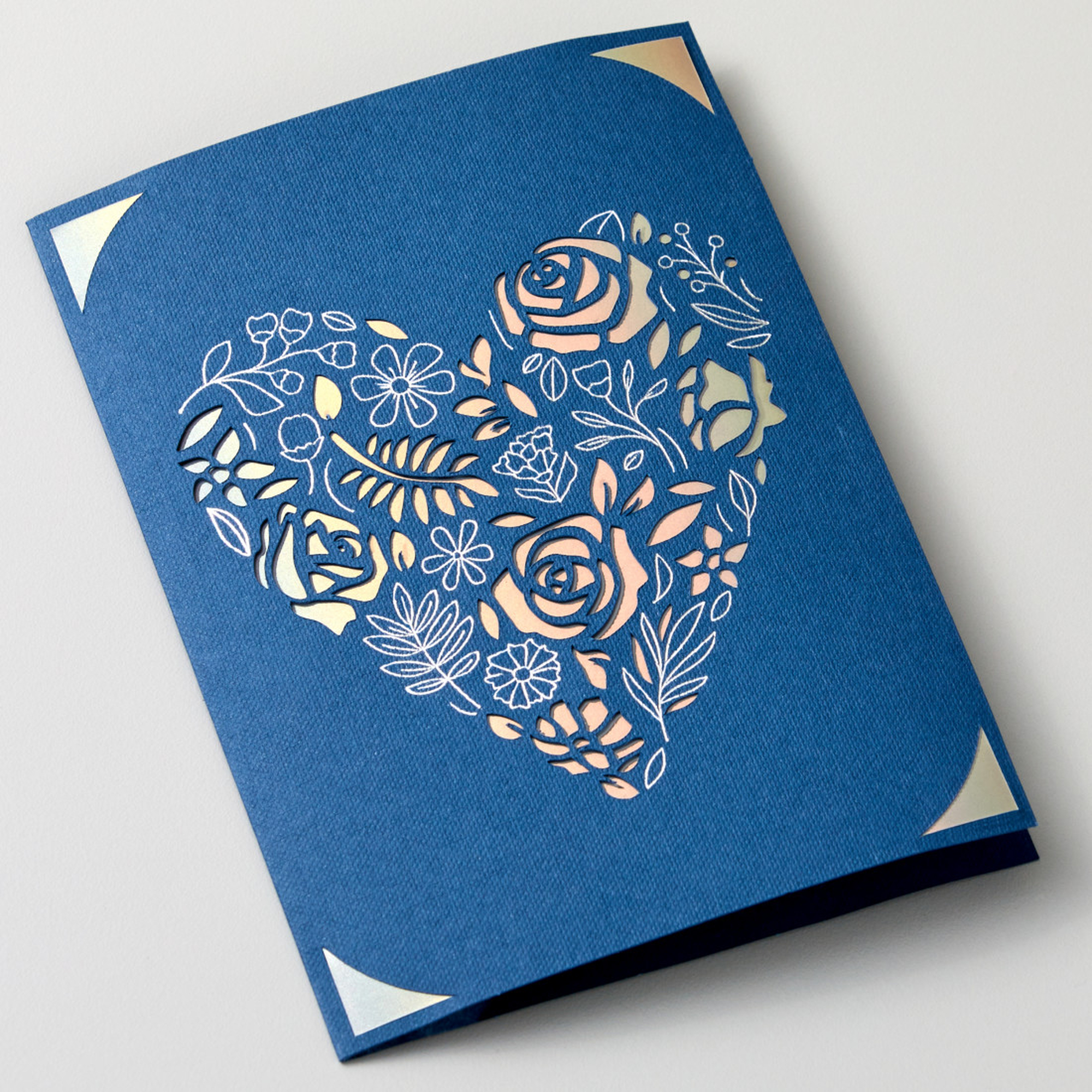 Blaue Karte mit herzförmigem floralem Ausschnitt, offen auf weißer Oberfläche.