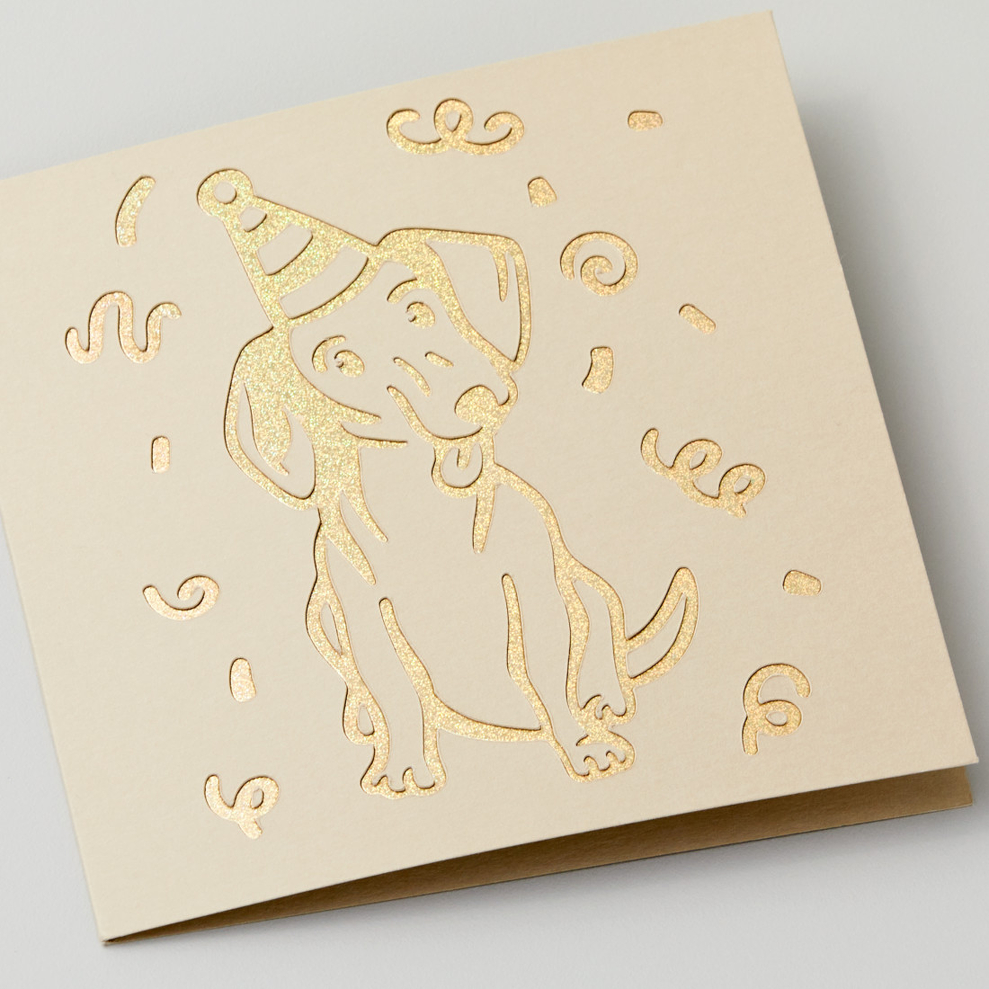 Eine Grußkarte mit goldenem Hund, Partyhut und Konfetti.