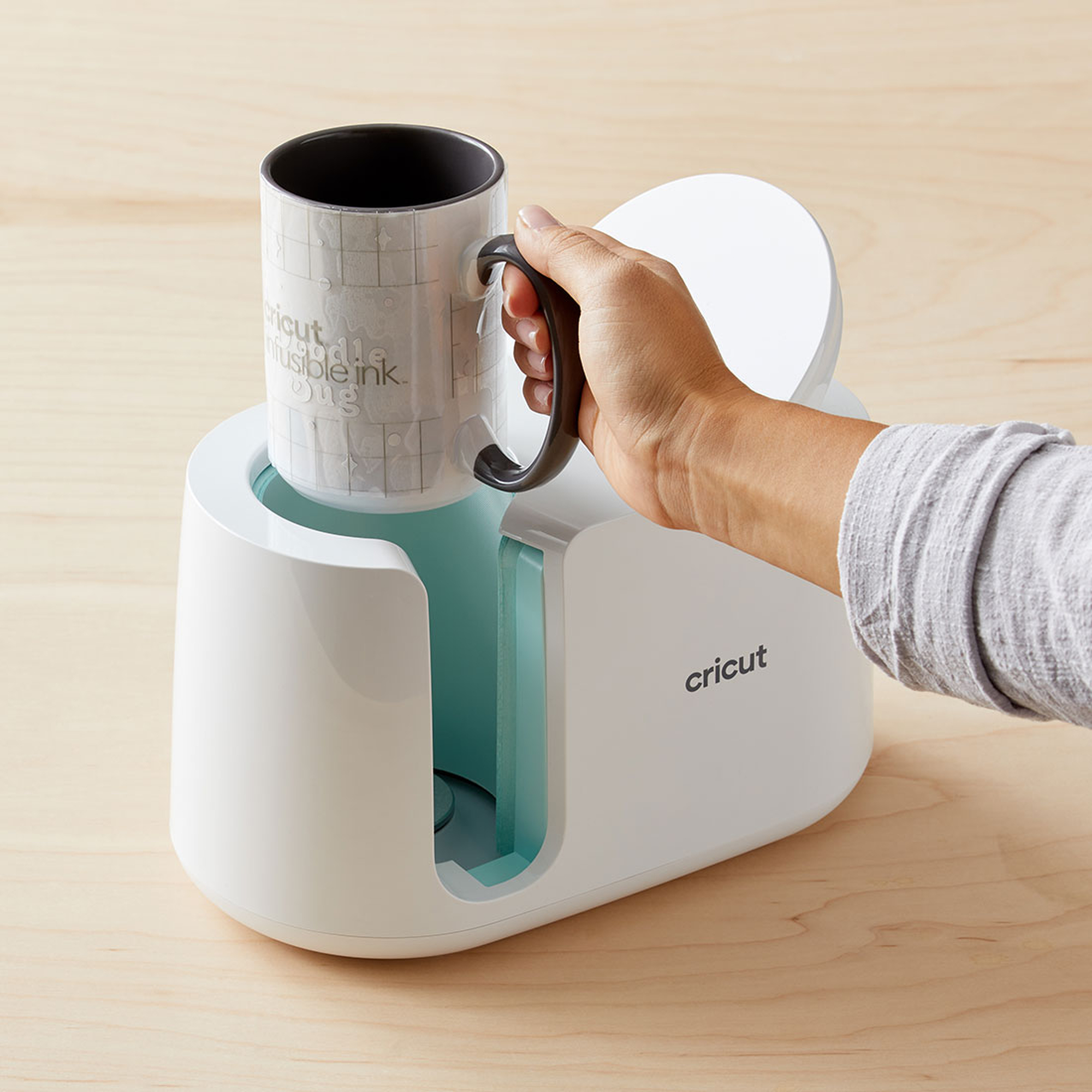 Eine Hand, die eine Tasse in einer Cricut-Tassenpressmaschine hält.