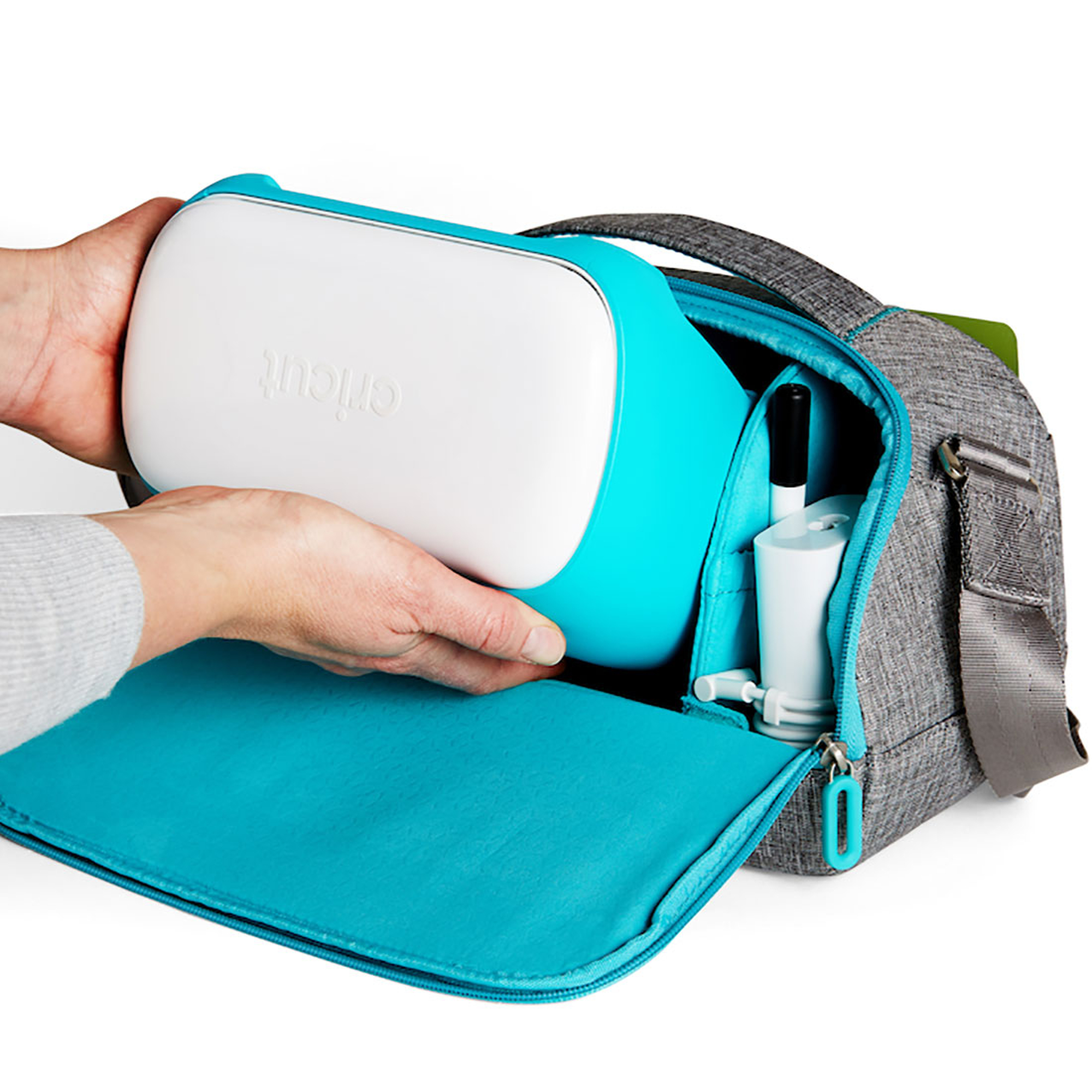 Person legt eine Cricut-Maschine in eine graue Tasche. Türkisgrüne Maschine und Tasche.
