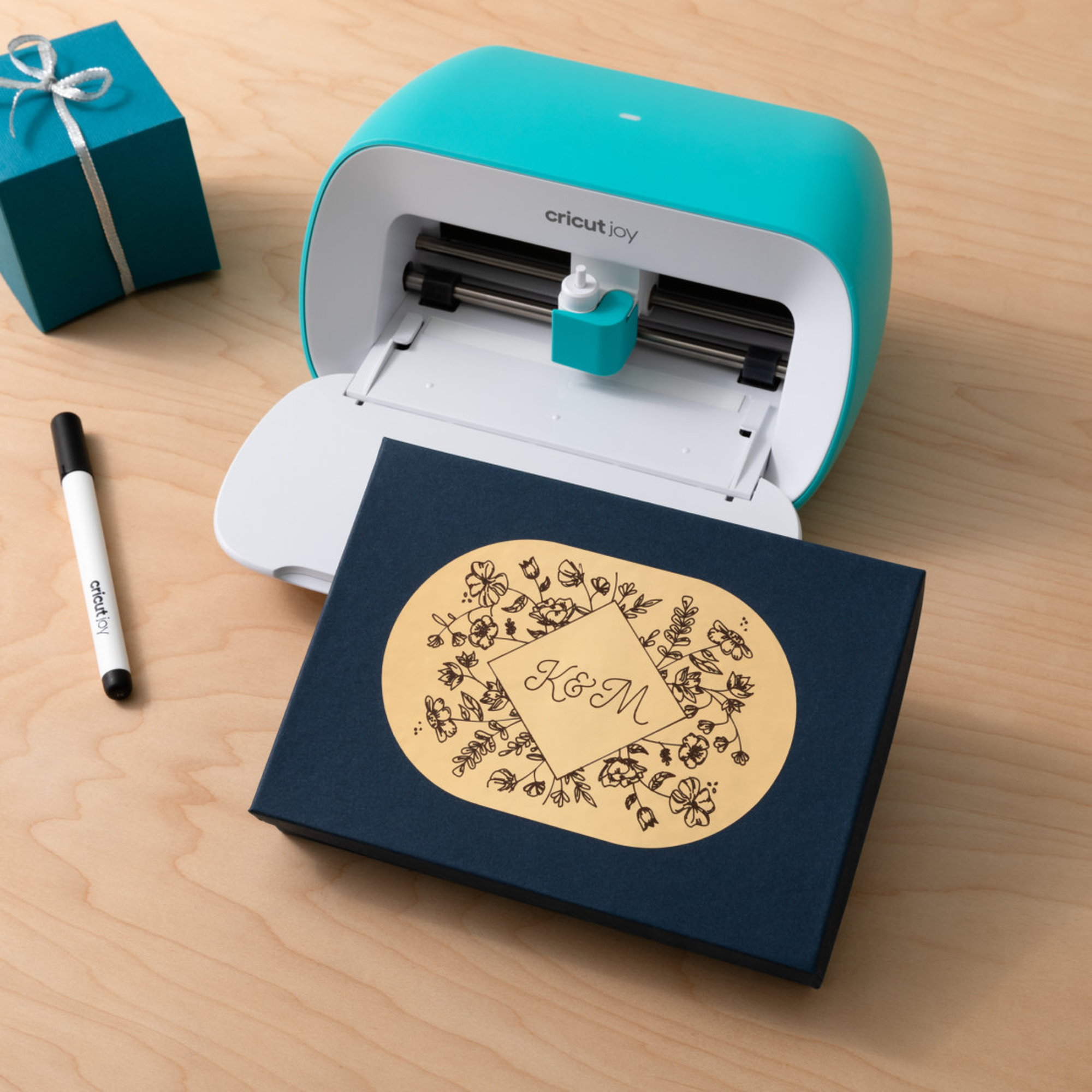 Eine blaue Bastelmaschine und Zubehör auf einer Holzoberfläche, auch eine Geschenkbox.