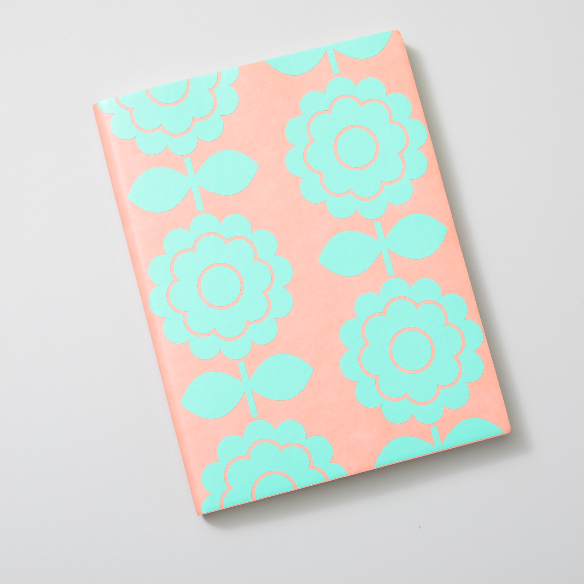Ein Notizbuch mit pfirsichfarbenem Einband. Der Einband hat ein Muster aus türkisfarbenen Blumen.
