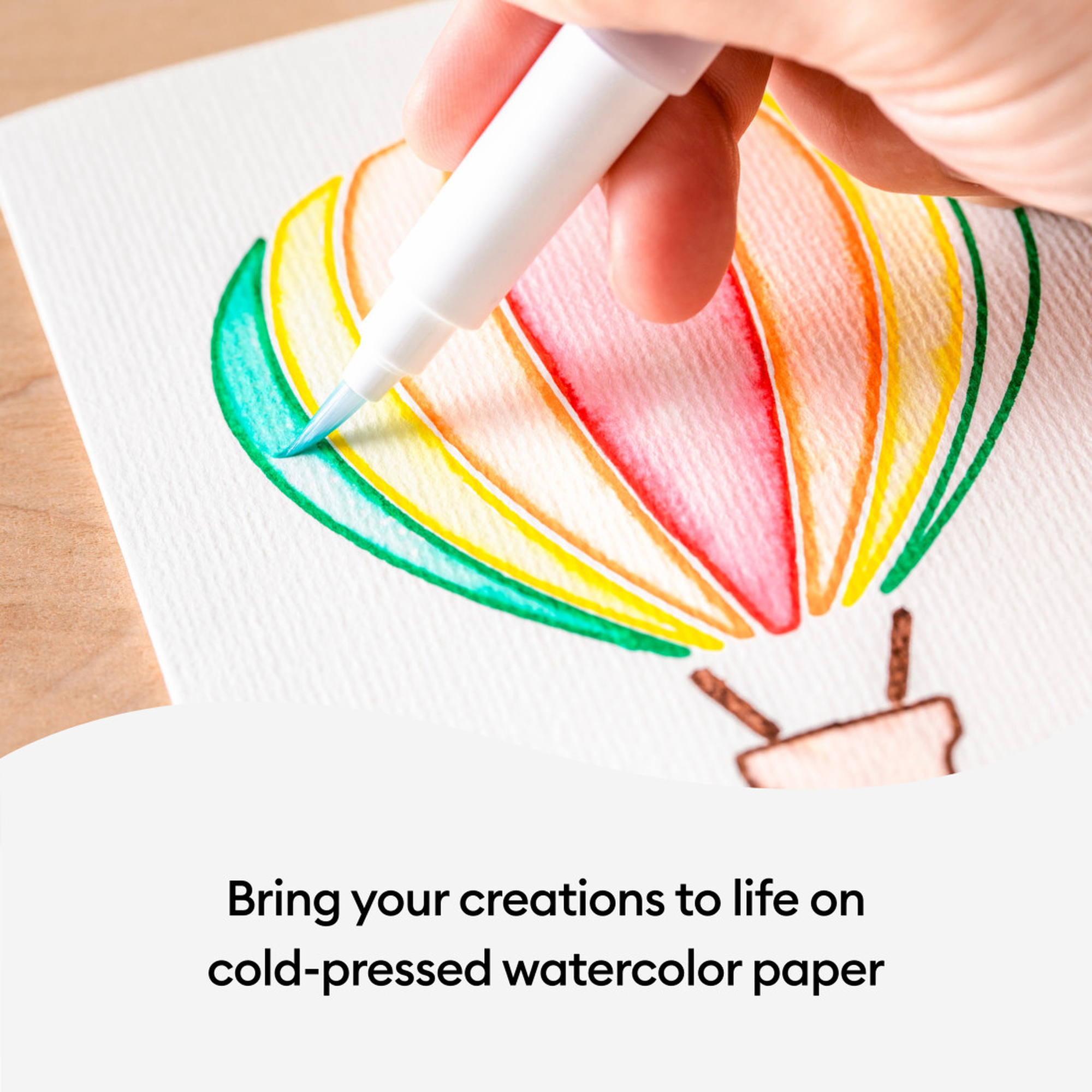 Eine Hand bemalt einen Heißluftballon mit Aquarellfarben. Text: 'Erwecken Sie Ihre Kreationen auf Aquarellpapier zum Leben'.