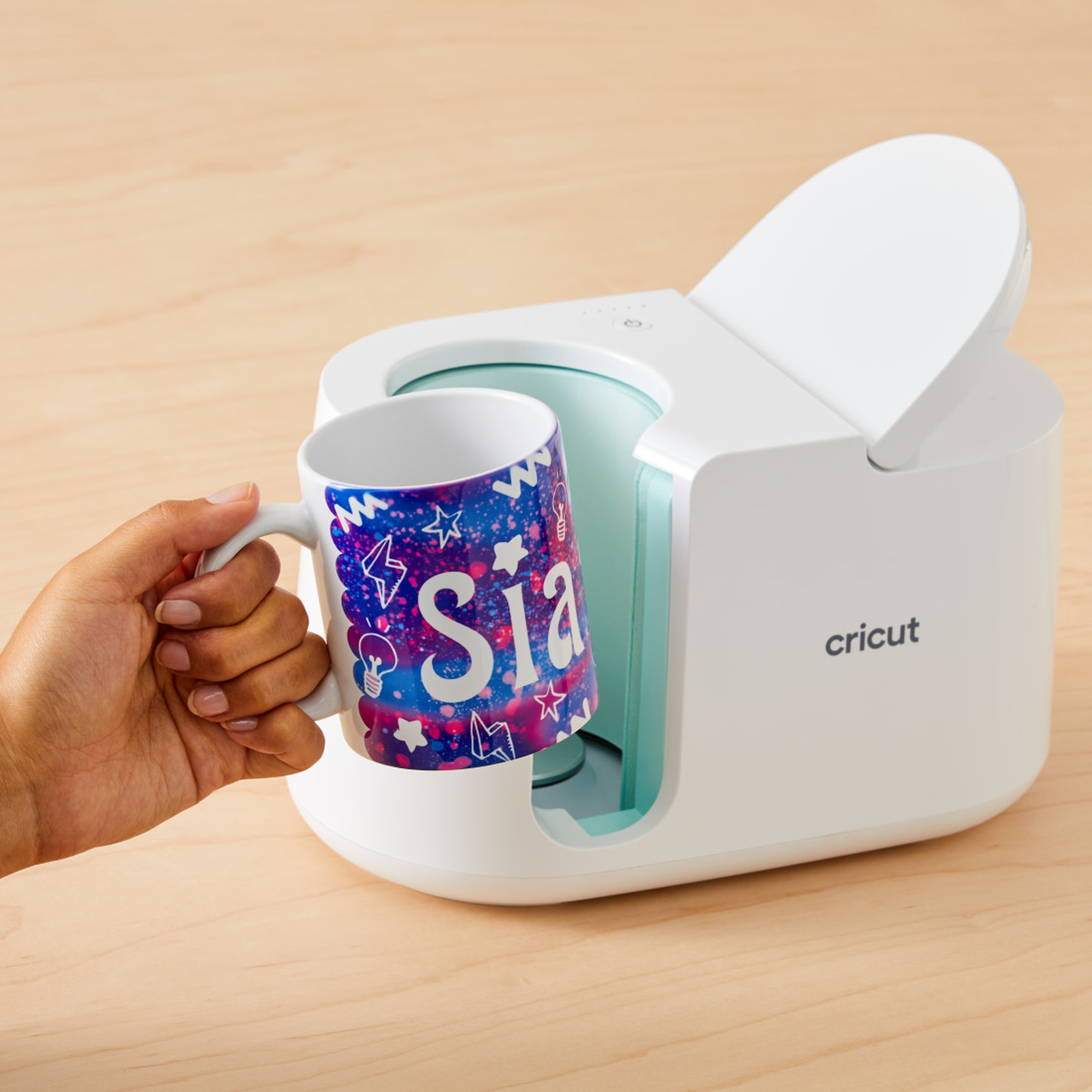 Eine Hand hält eine Tasse mit dem Namen 'Sia', und eine Cricut-Tassenpresse befindet sich daneben.