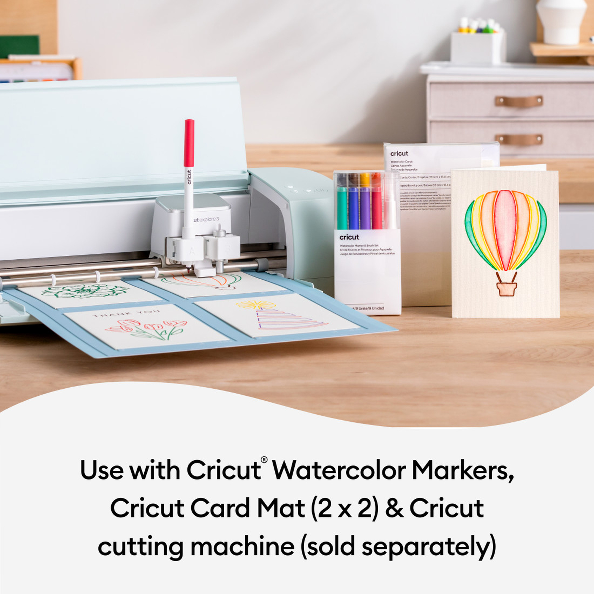 Cricut-Schneidemaschine mit Karten. Roter Stift, Marker und eine Ballonkarte auf einem Holztisch.