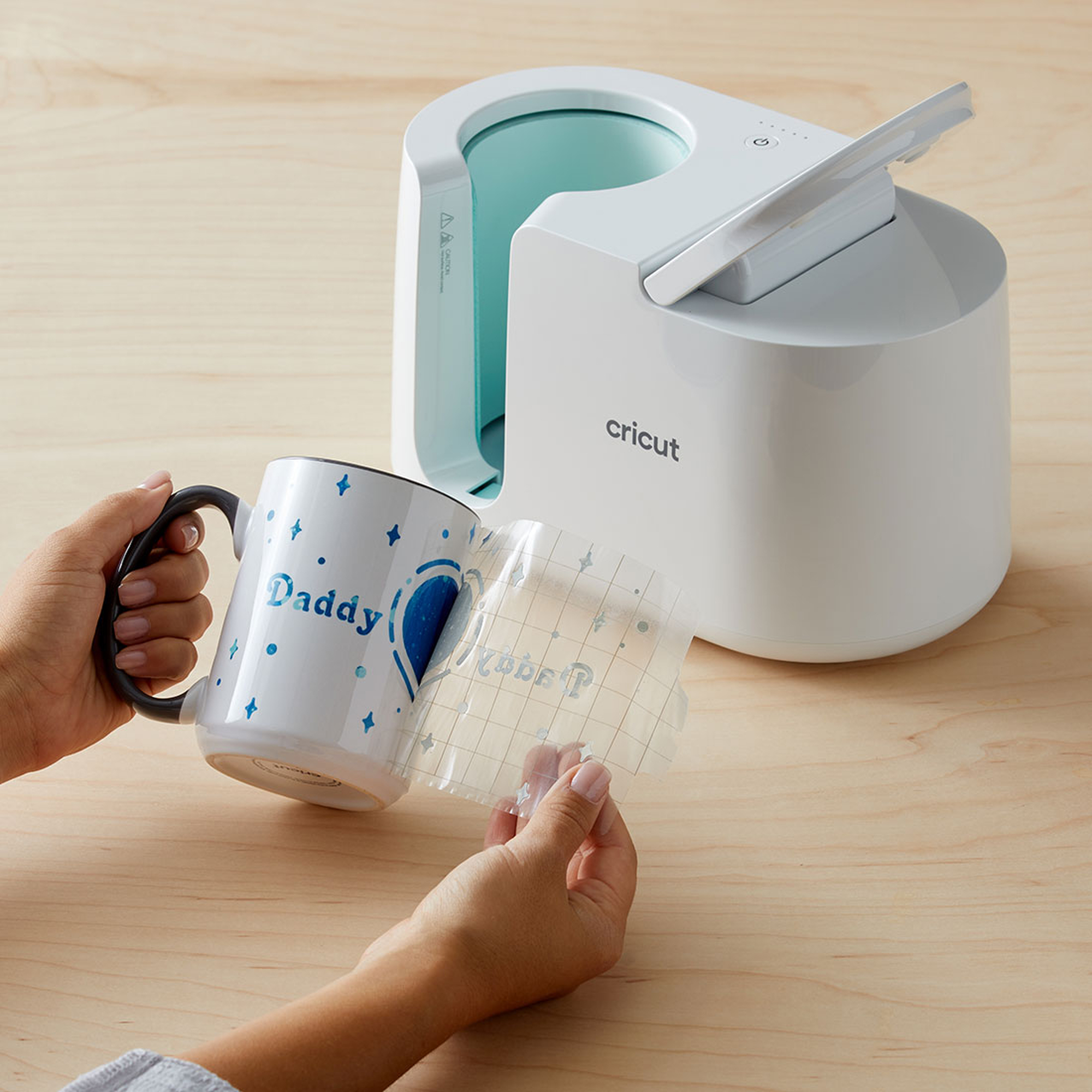 Eine Cricut-Tassenpresse mit einer Tasse und einem Design, das angebracht wird, zeigt den Druckvorgang.