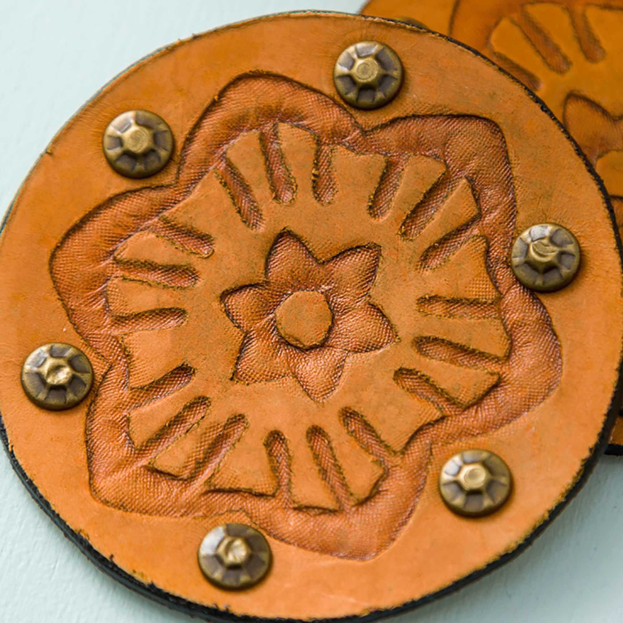 Zwei Lederuntersetzer mit Blumendesigns und Nieten. Braune Farbe.