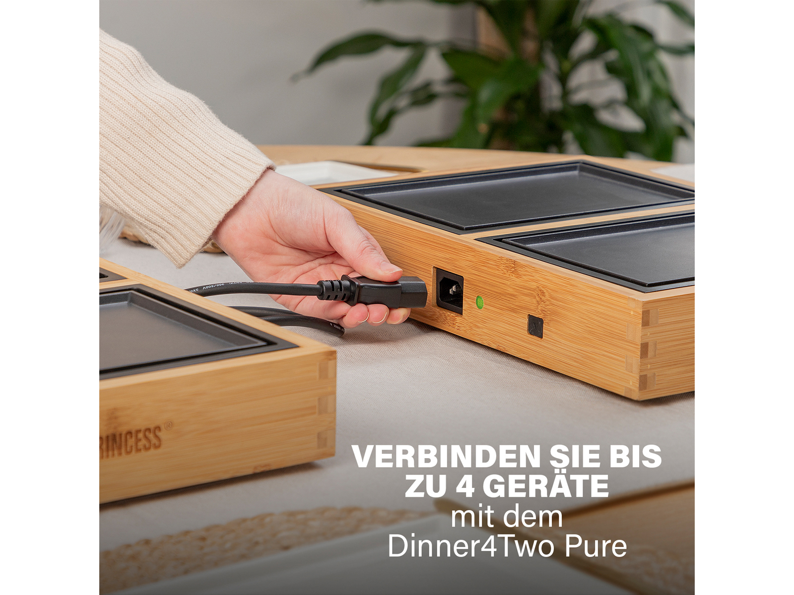 Eine Person steckt ein Kabel in ein Kochgerät im Bambus-Stil. Text sagt 'Verbinden Sie bis zu 4 Geräte'.