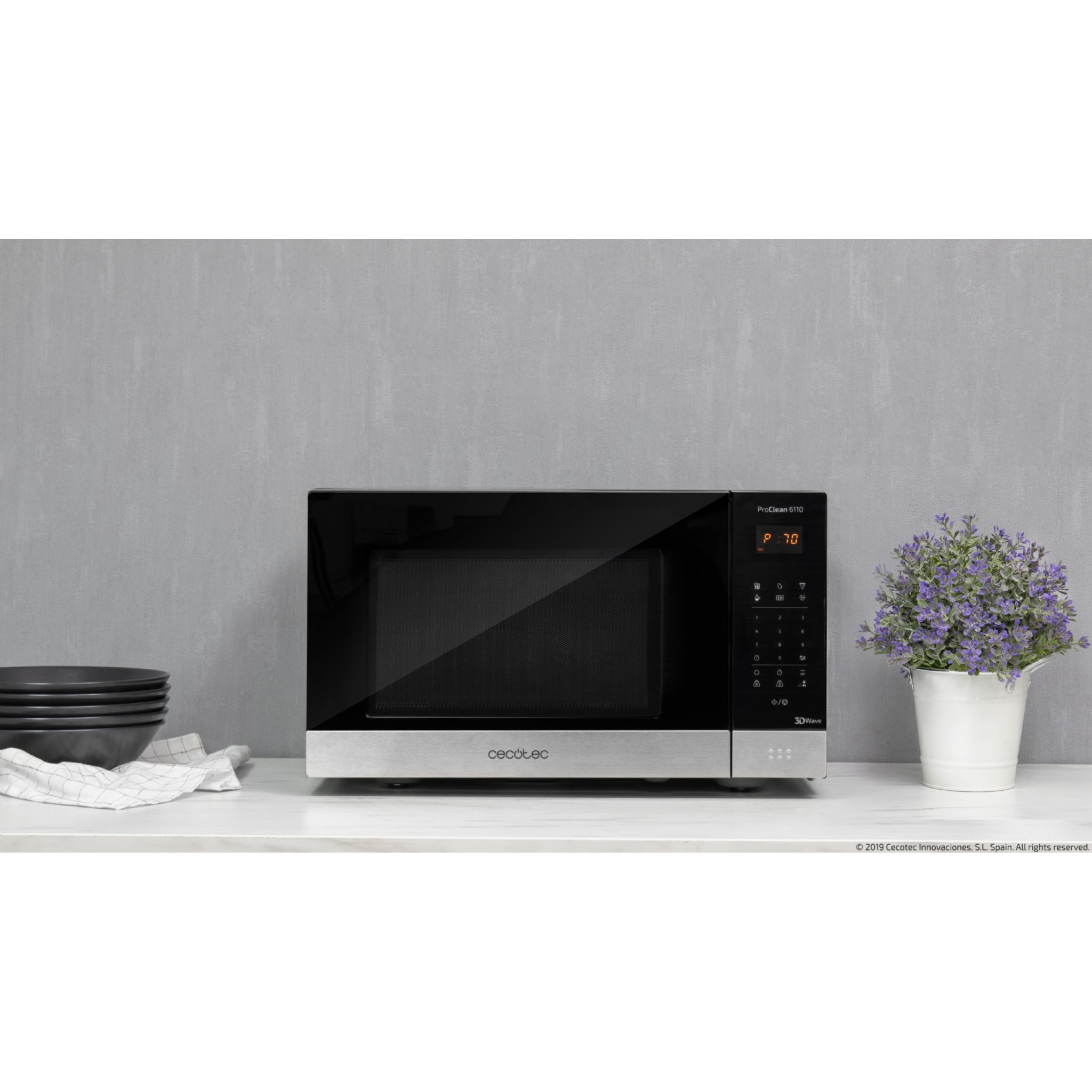 Czarna kuchenka mikrofalowa ze srebrną podstawą, na białym blacie z doniczką.