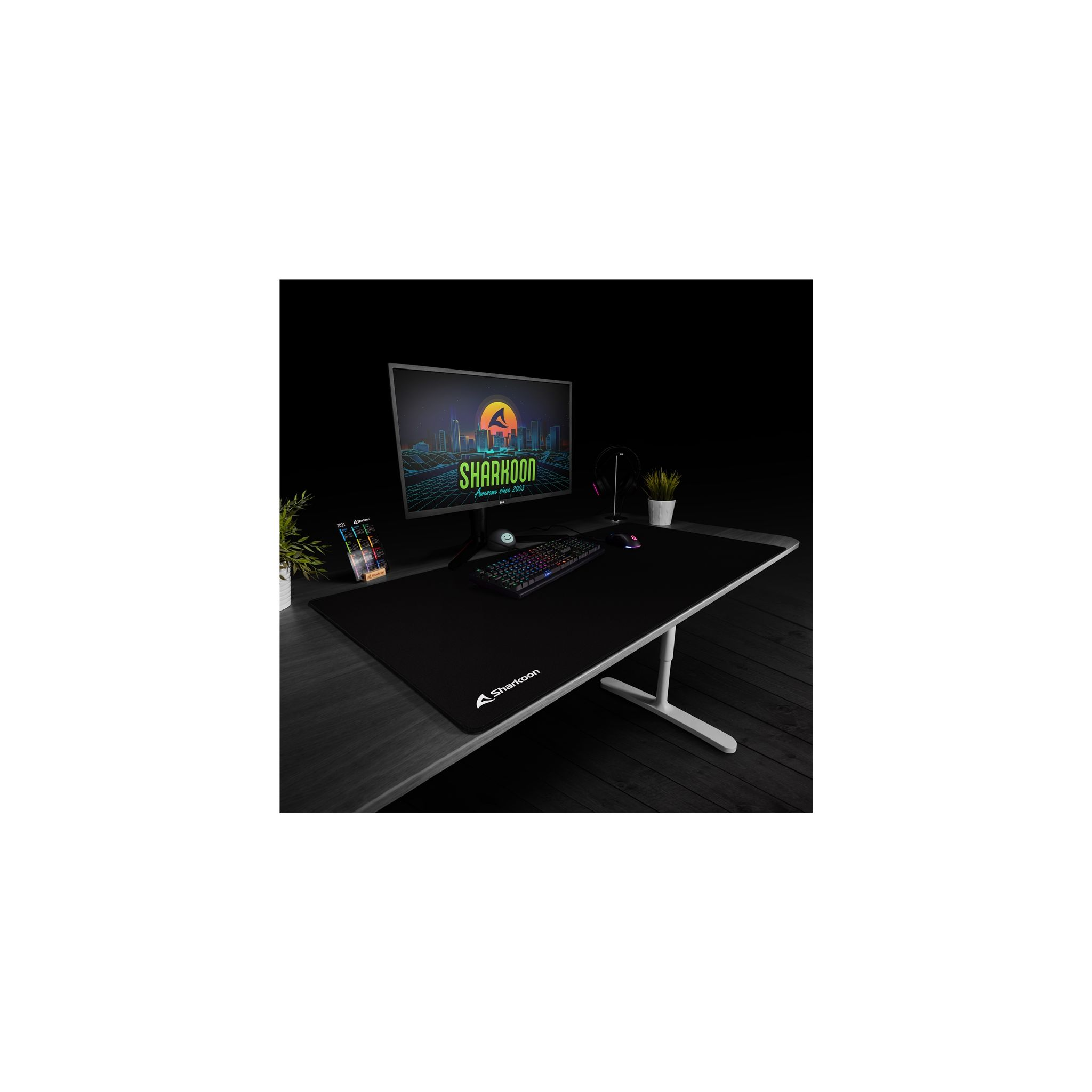 Configuration de bureau noire avec un moniteur, un clavier, une souris et une plante. Texte Sharoon sur le tapis.