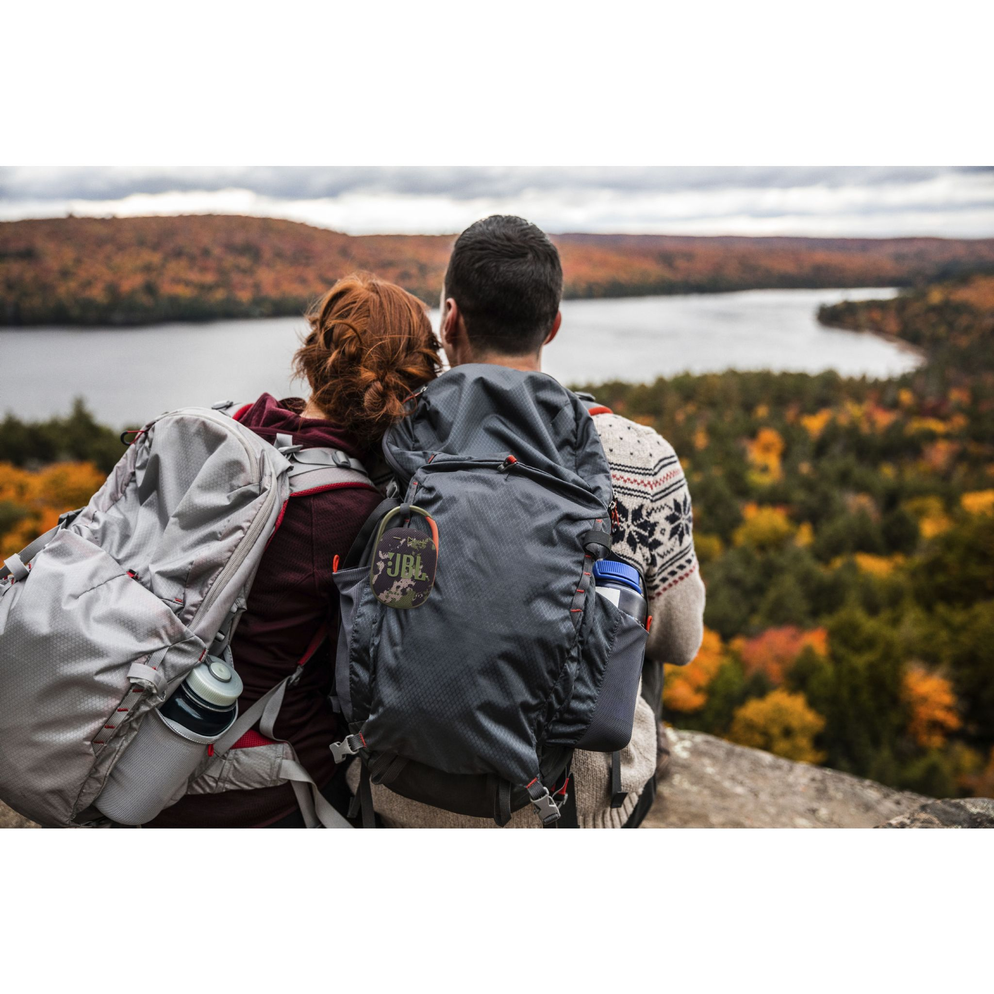 Dos excursionistas con mochilas contemplan un lago rodeado de follaje otoñal.
