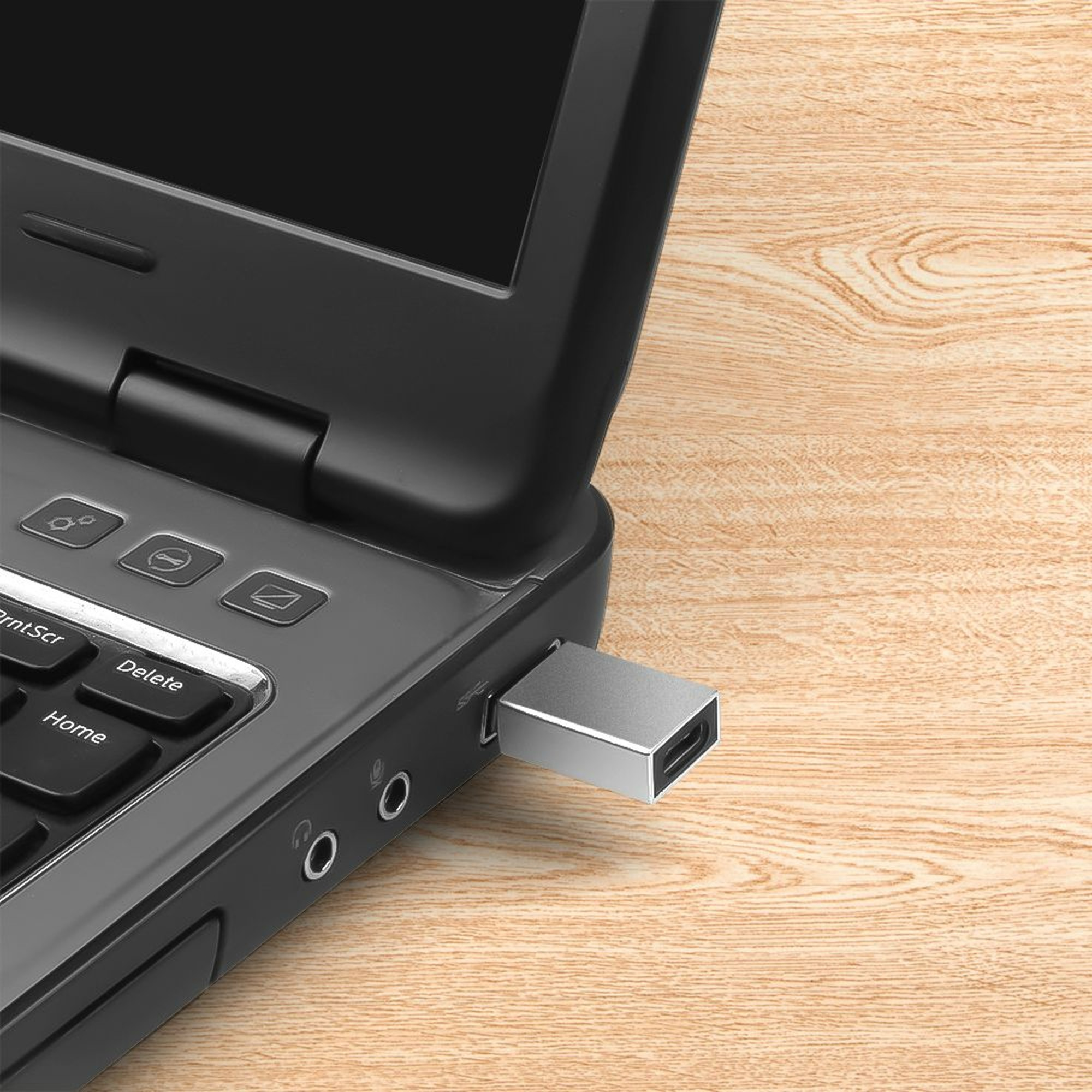Silberner USB-Stick in einen schwarzen Laptop gesteckt, auf einem Holztisch liegend.