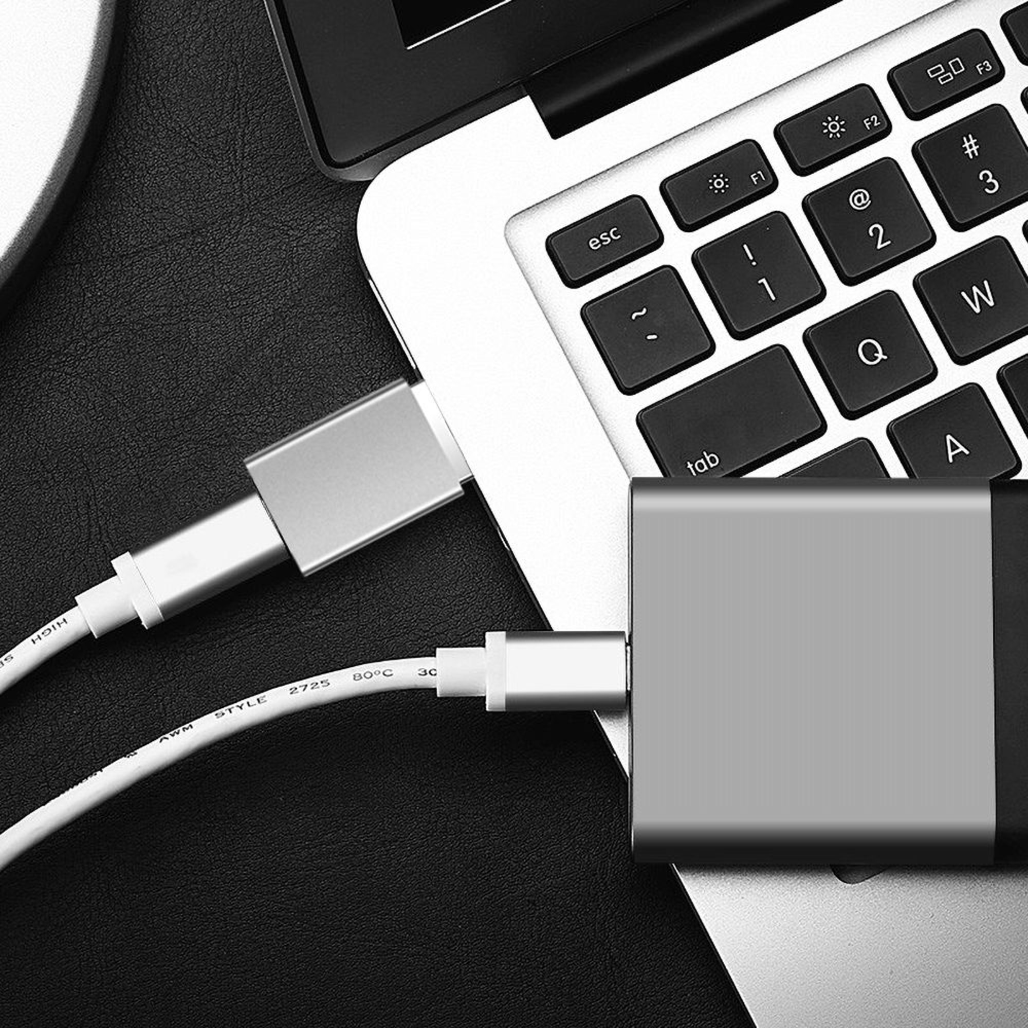 Laptop mit Kabeln, die an einen silbernen Hub und einen USB-C-Adapter angeschlossen sind, auf schwarzem Untergrund.