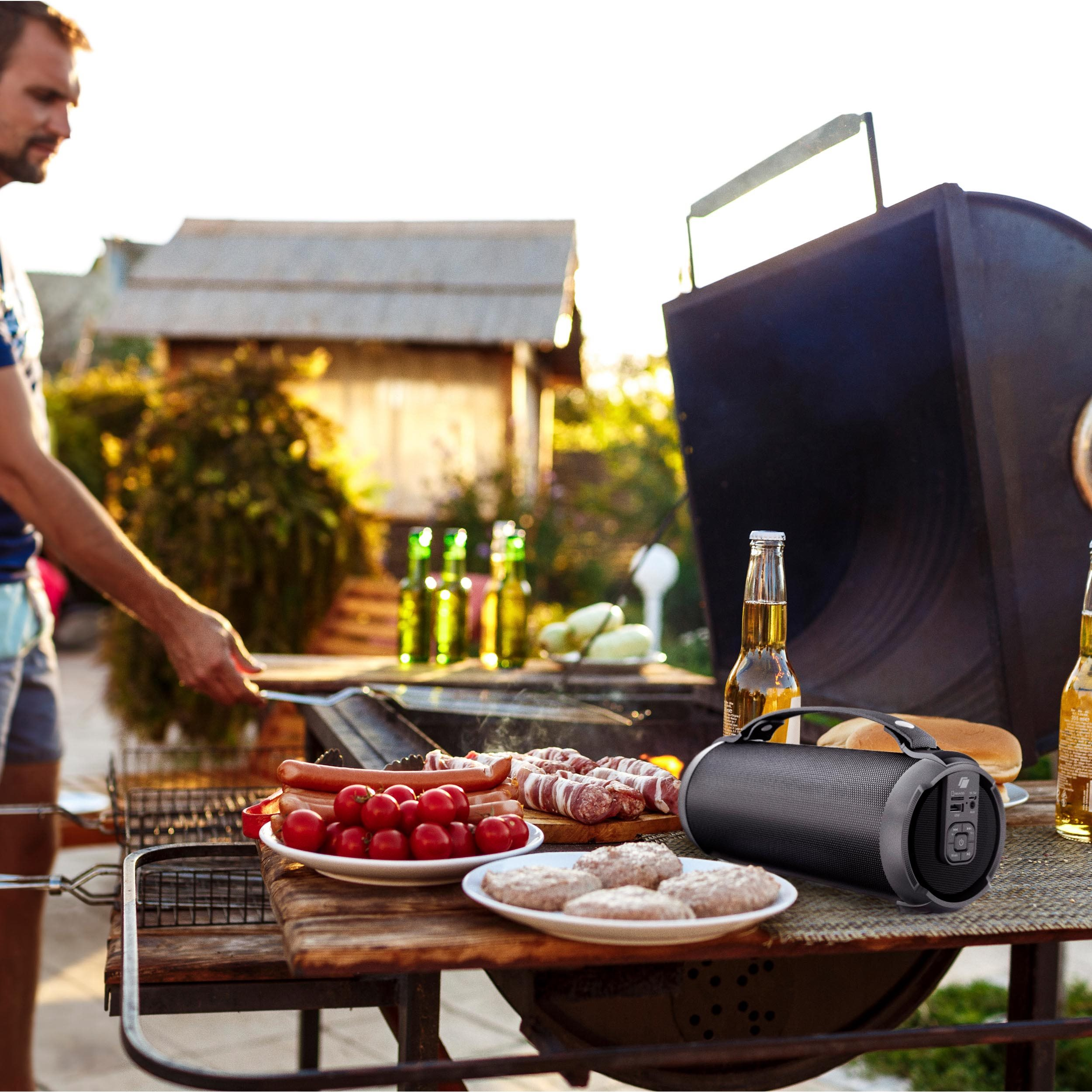 Mann grillt Essen mit tragbarem Lautsprecher, Bier und Essen auf einem Holztisch.