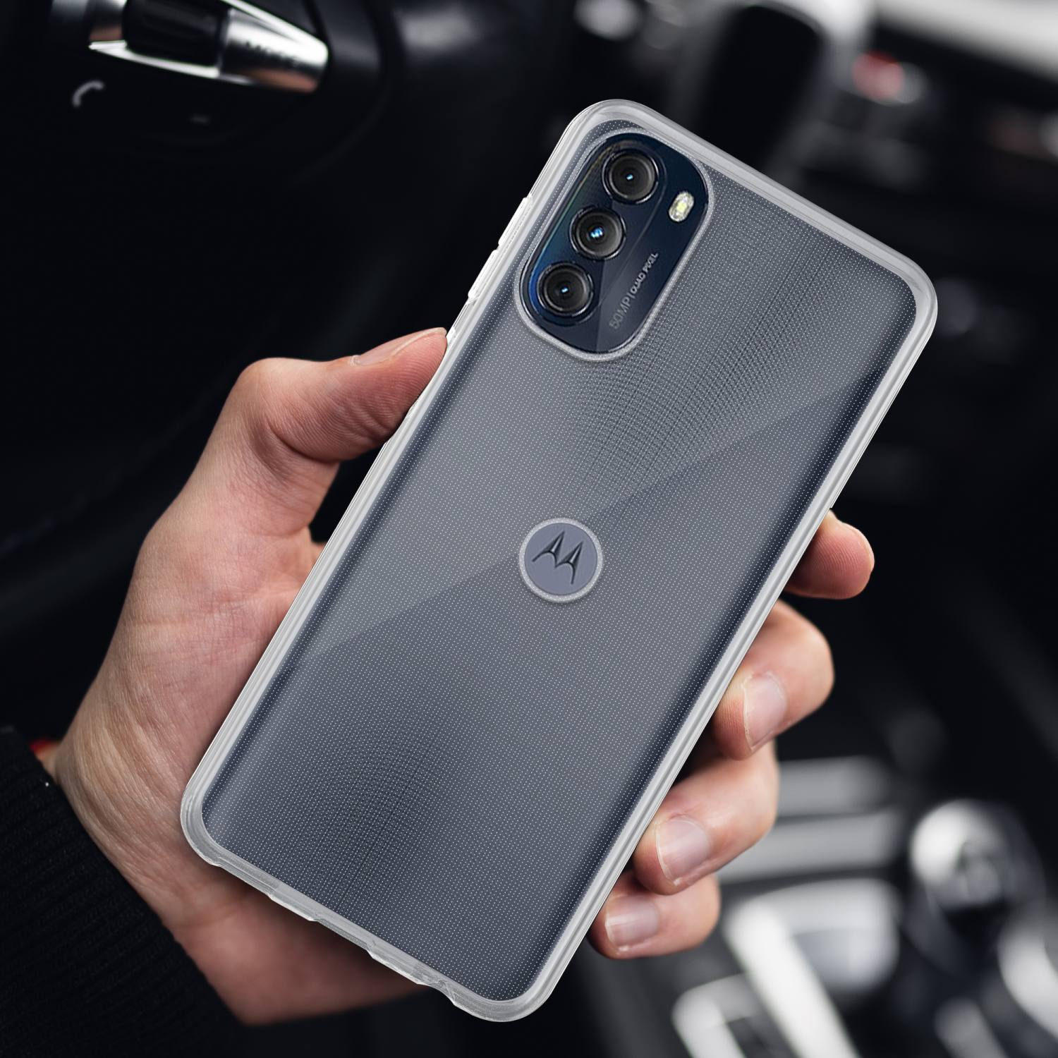 Mano che tiene una custodia trasparente sopra un telefono. Un interno auto è sullo sfondo.