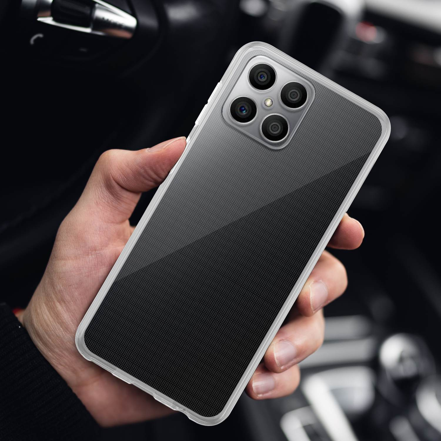 Eine Hand, die ein Telefon mit durchsichtiger Hülle hält. Der Hintergrund ist ein dunkler, verschwommener Innenraum.