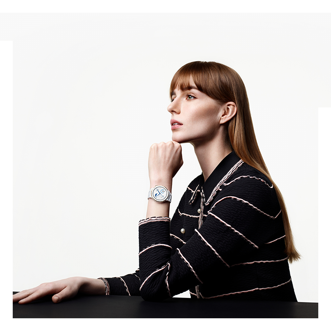 Donna che guarda altrove con un orologio. Camicia a righe bianche e nere.