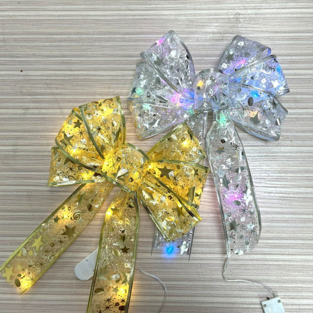 Zwei dekorative Weihnachtsschleifen mit Lichtern, eine goldene und eine silberne, auf Holzmaserung.