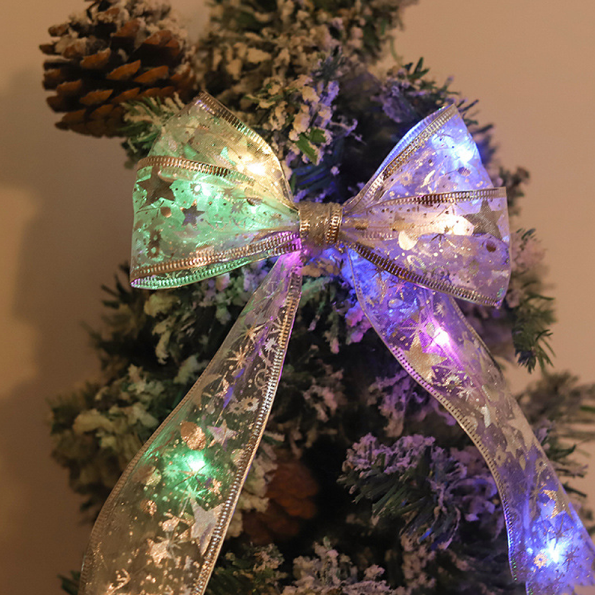 Weihnachtsschleife mit Lichtern. Silbernes Band, mit Schneeflocken und Sternen. Grün und blau leuchtend.