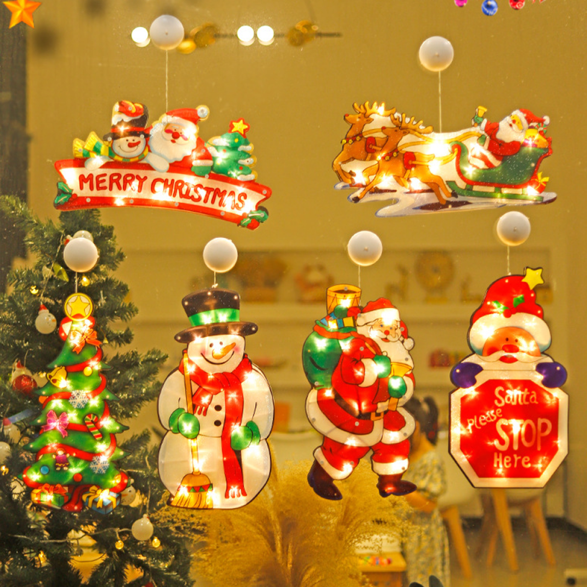 Weihnachtsdekorationen am Fenster: Weihnachtsmann, Schneemann und Merry Christmas-Schild. Ein Weihnachtsbaum sichtbar.